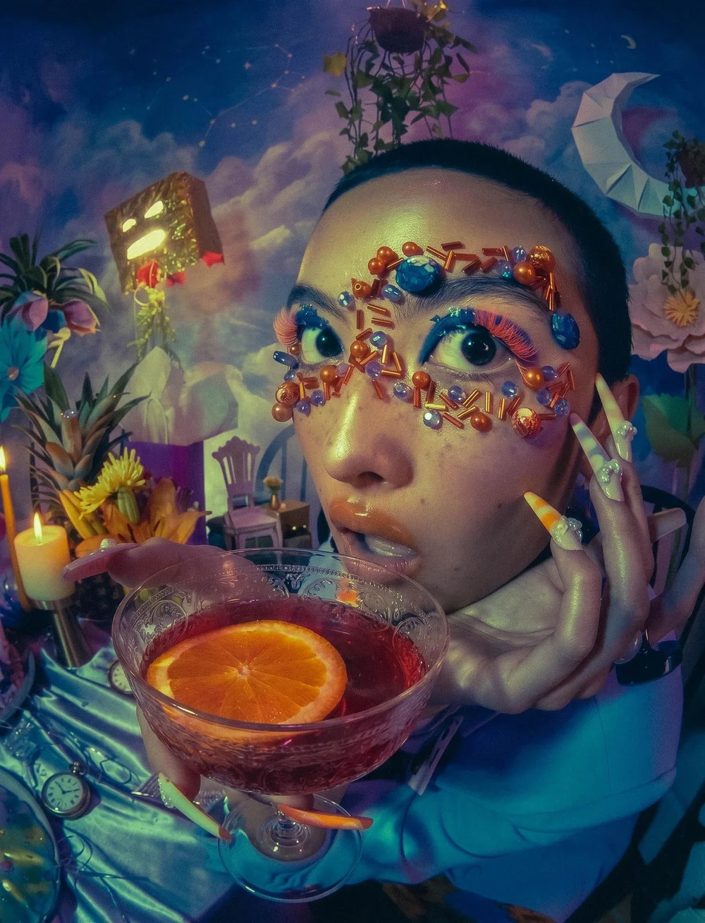 Person with elaborate makeup and jewelry holding a drink with an orange slice, surrounded by colorful, surreal background elements.