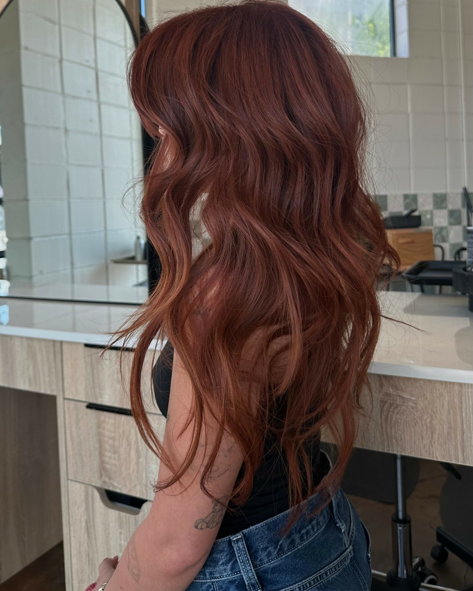 Side view of a person with long, wavy, reddish-brown hair in a kitchen.