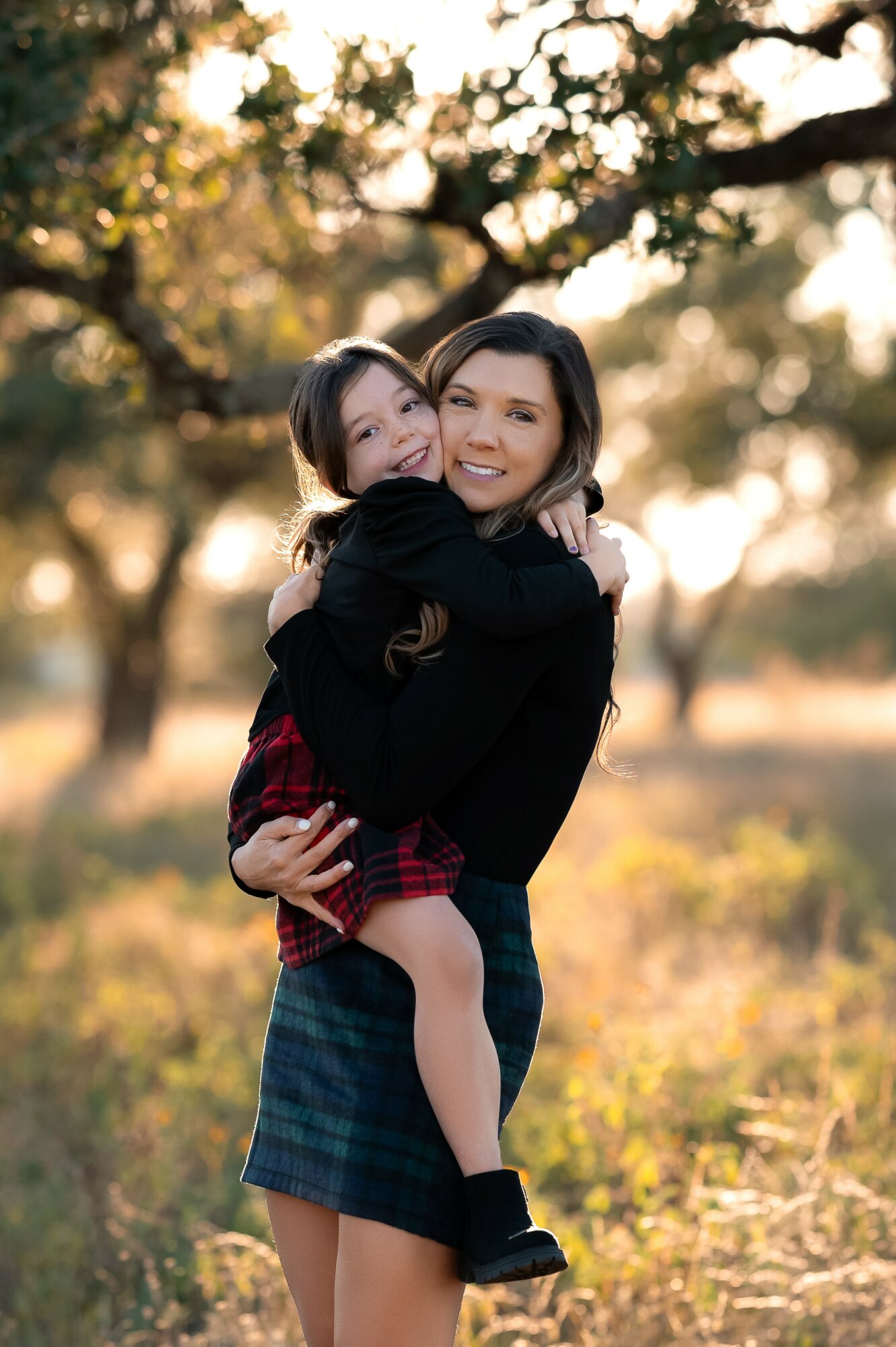 Two people hugging outdoors in a park with trees and sunlight, smiling happily.