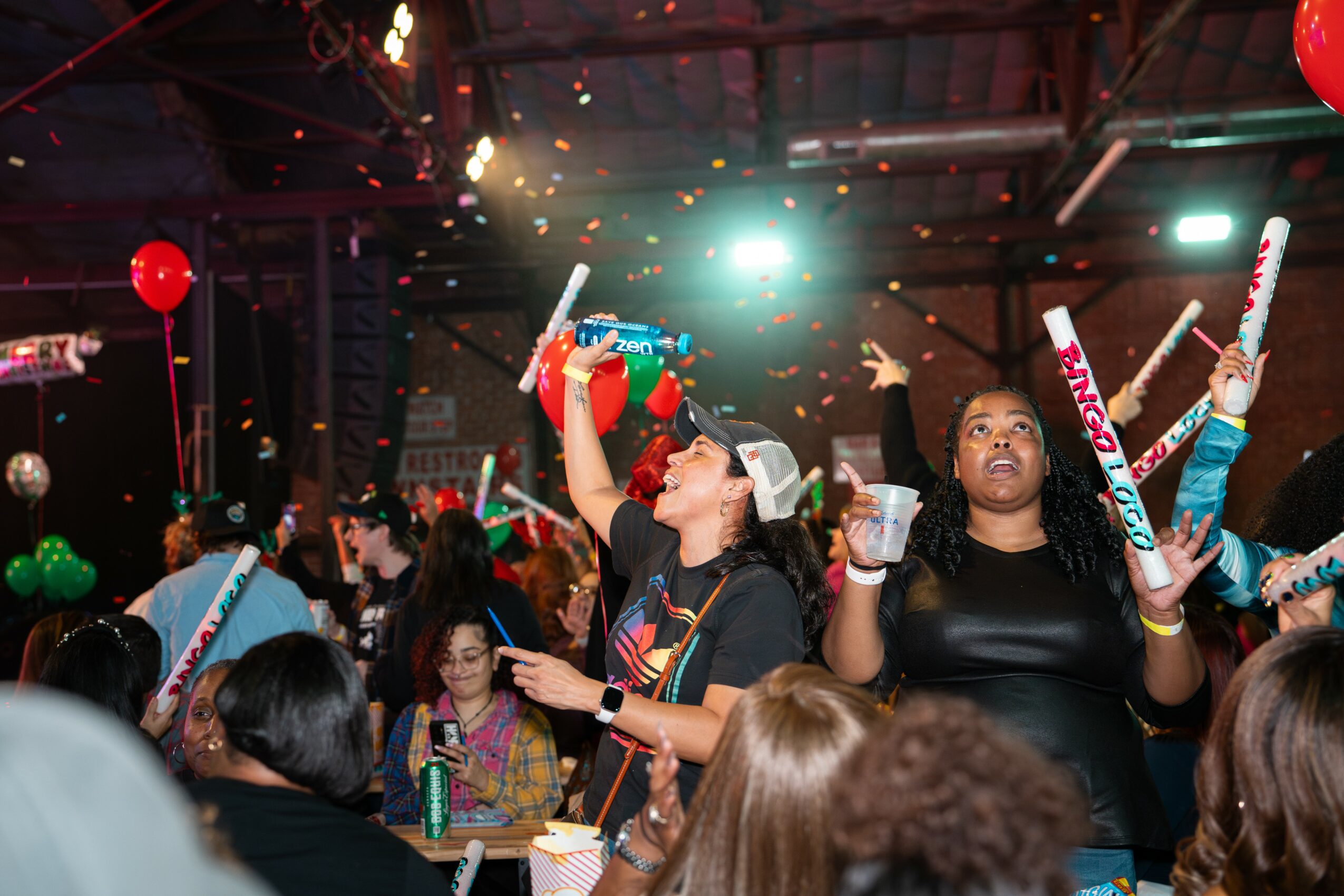 People celebrating with party hats, balloons, and confetti in a festive indoor setting.