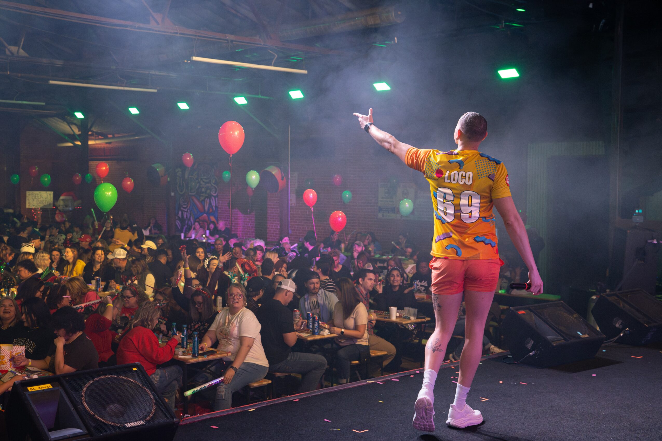 Performer on stage with a crowd, colorful balloons, and stage lights in the background.