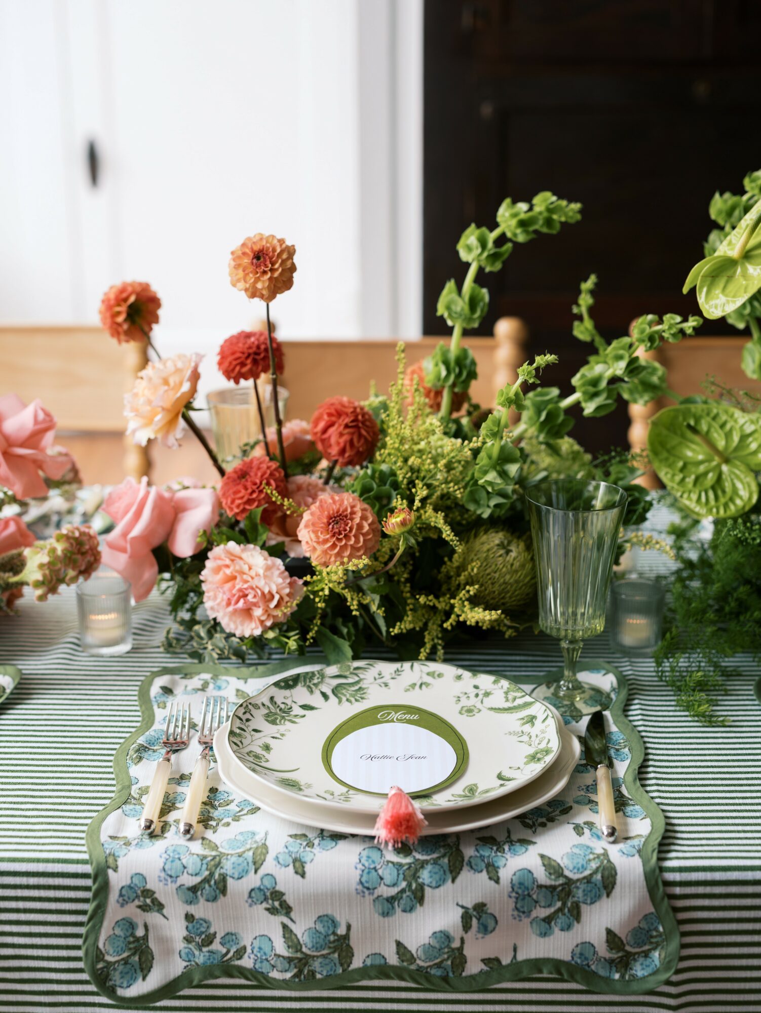 Table setting with floral centerpiece, patterned tablecloth, plate, fork, knife, and glass, in a bright room with white and dark background.
