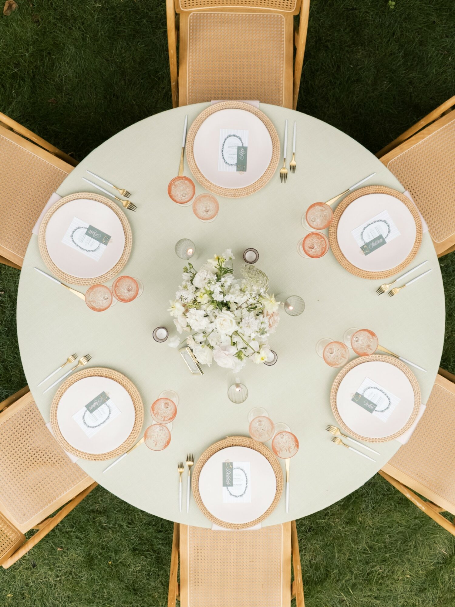Round table set with six place settings, a floral centerpiece, and glasses, chairs around the table, outdoor setting