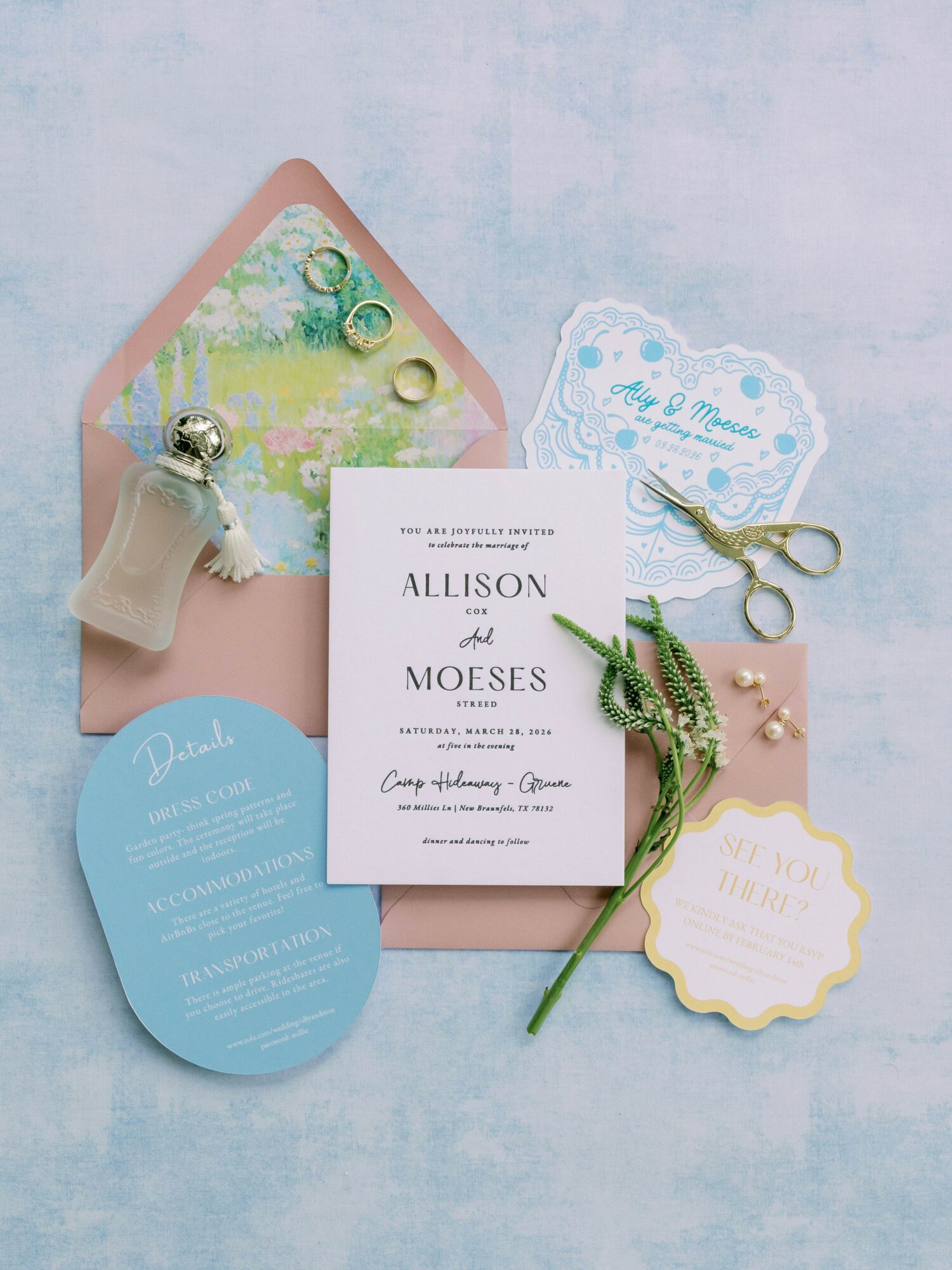 Wedding invitation, envelope, and decorative items arranged on a light blue surface, including scissors, a small bottle, and a flower.