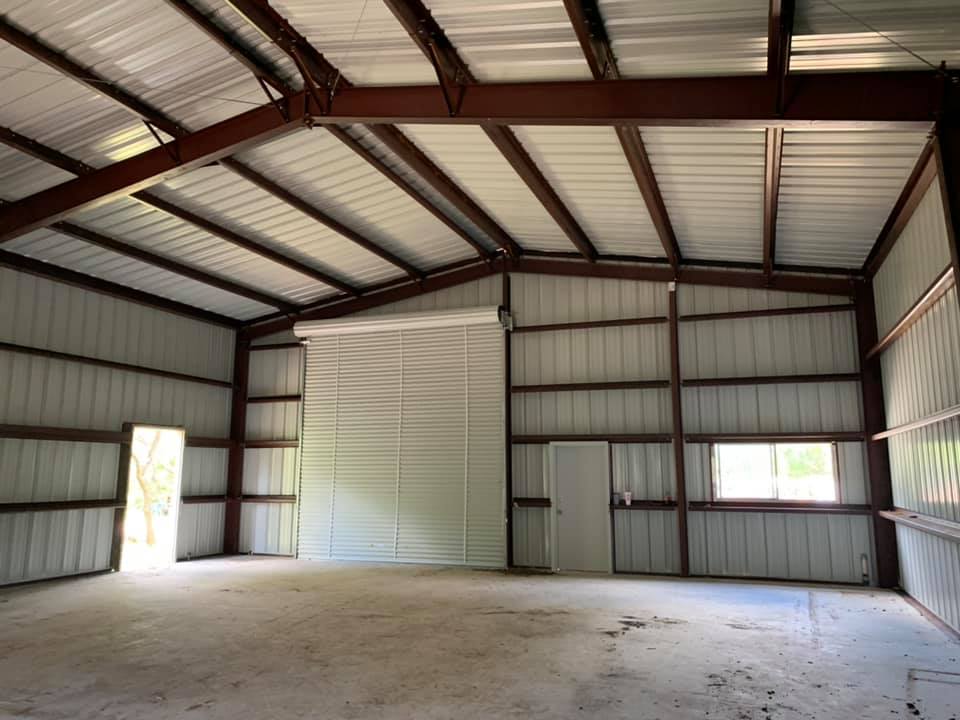 Interior of a large metal warehouse with high ceiling, metal walls, and a concrete floor, featuring a large sliding door and a window.