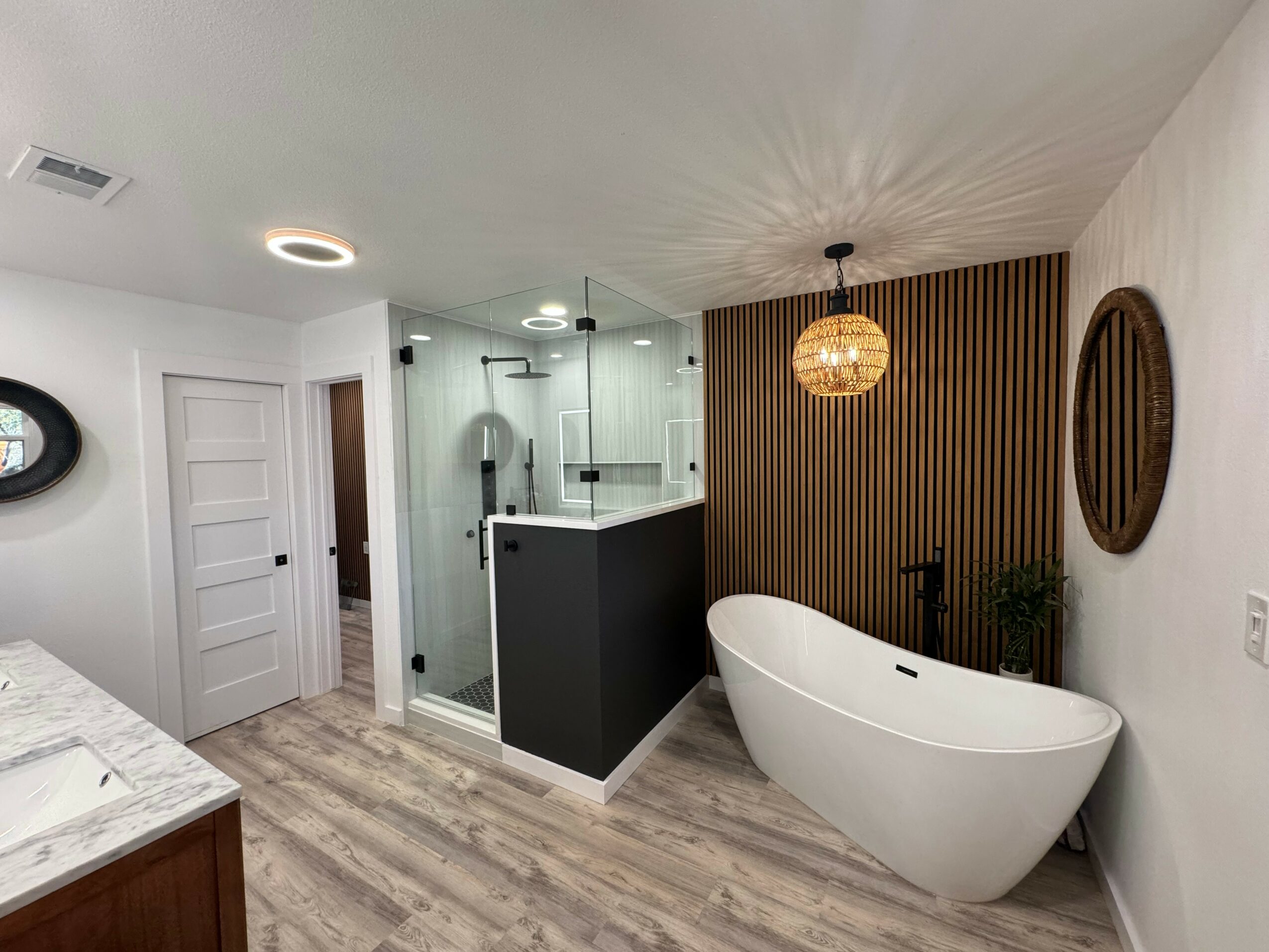 Bathroom with freestanding bathtub, wooden wall, glass shower, and modern decor, viewed from the doorway.