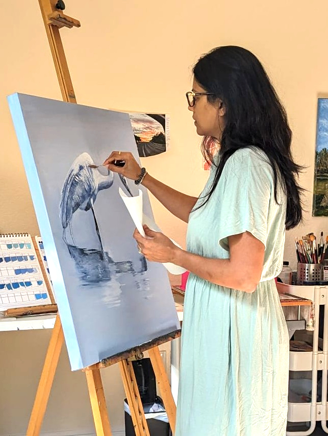 Woman painting a seascape with a whale on canvas, standing in an art studio, holding a palette and brush.