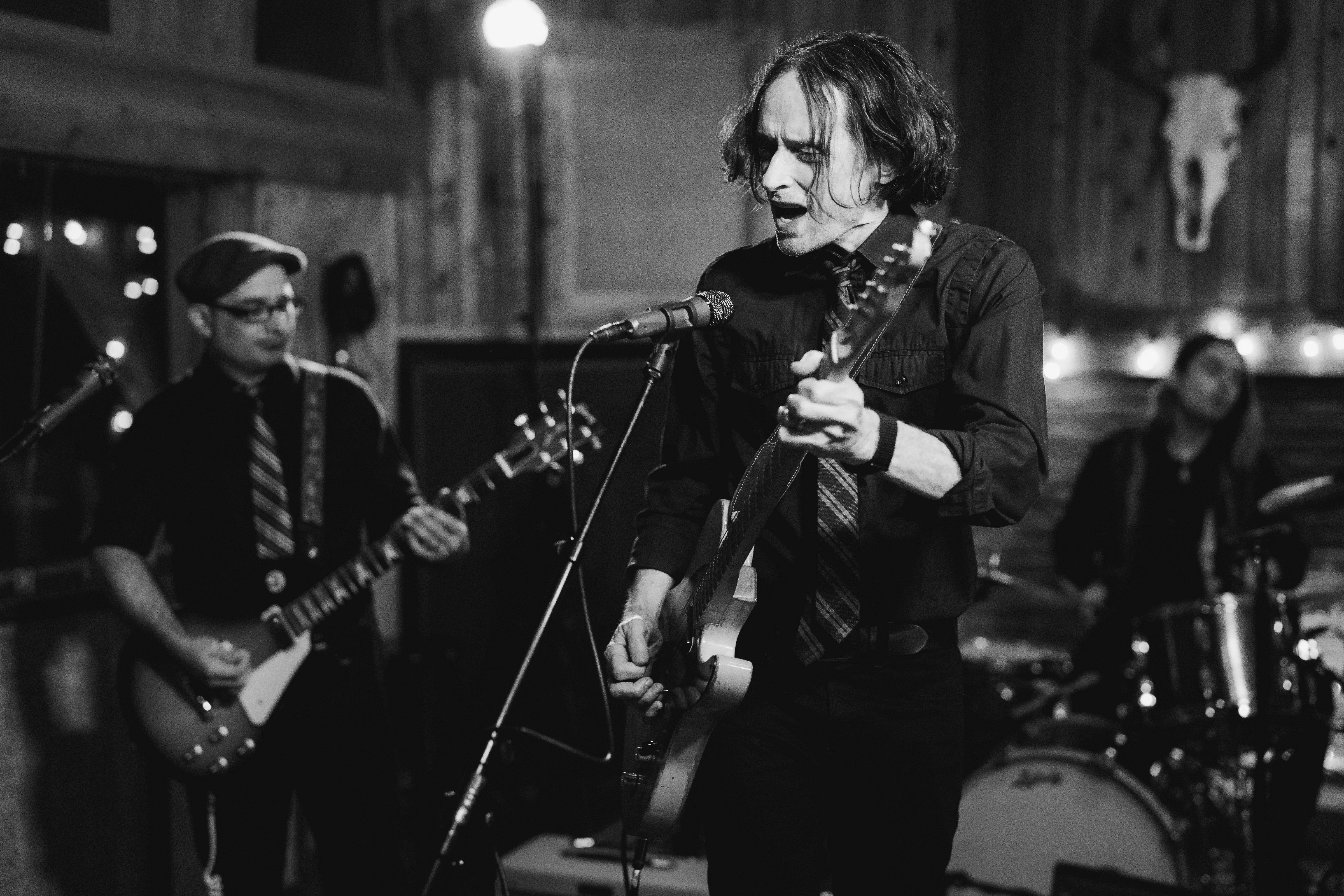 Black-and-white photo of a band performing, with a guitarist singing into a microphone and a drummer behind him.