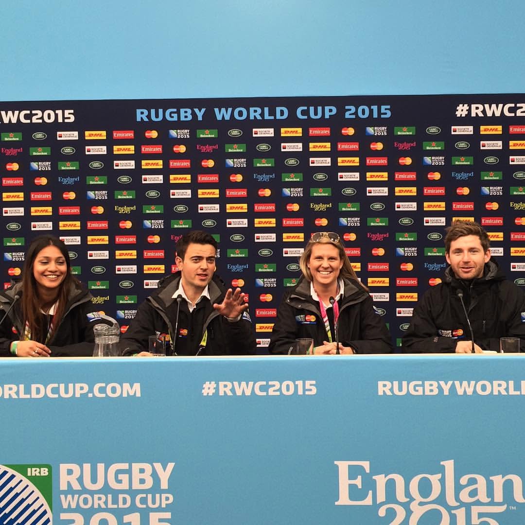 Four people sitting at a press conference table with a backdrop of sponsor logos and a blue banner reading Rugby World Cup 2015.