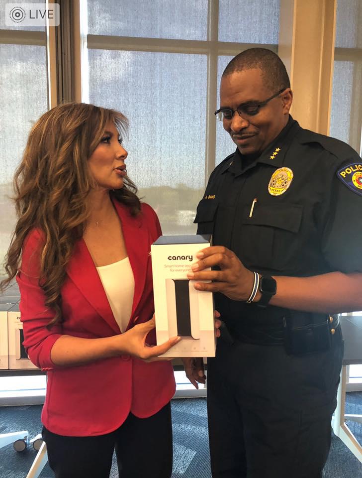 Woman in red blazer and police officer exchanging a boxed item indoors near windows.