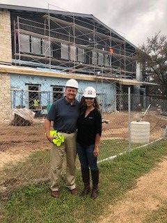 Two people standing outdoors near a construction site with a building under construction in the background.