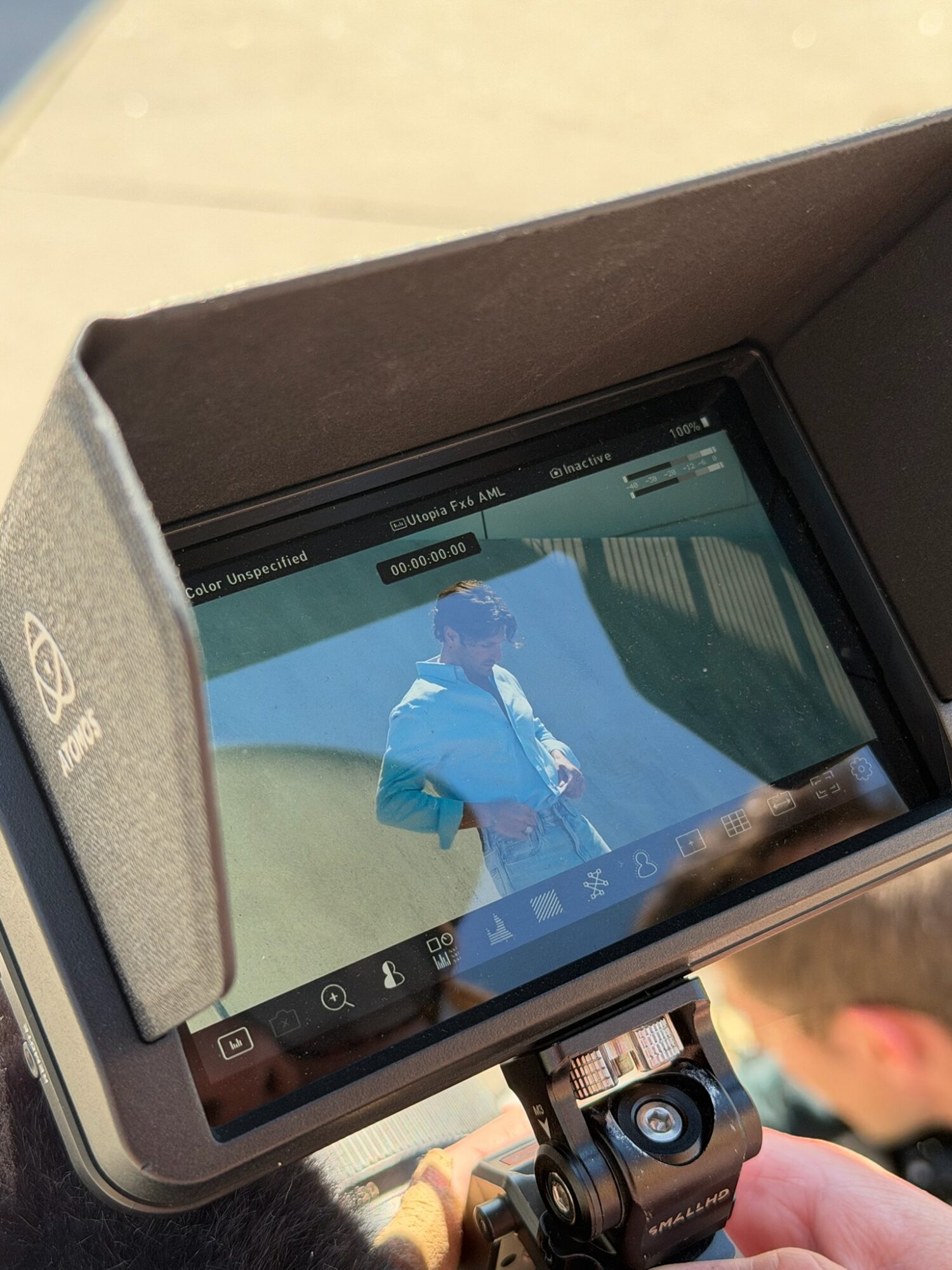 A person holding a camera with a screen displaying a person in a blue jacket, reflected in the camera's viewfinder.