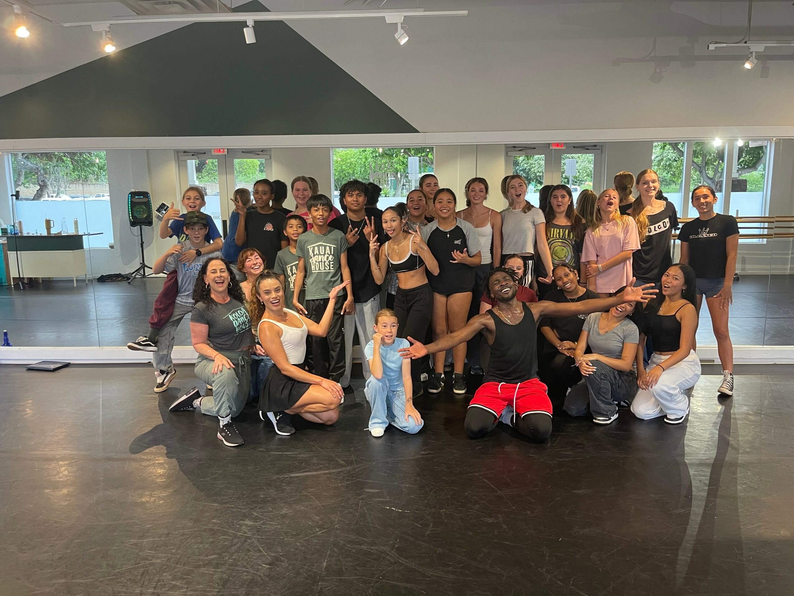 Group of people posing in a dance studio with mirrors and windows, some smiling and making gestures.