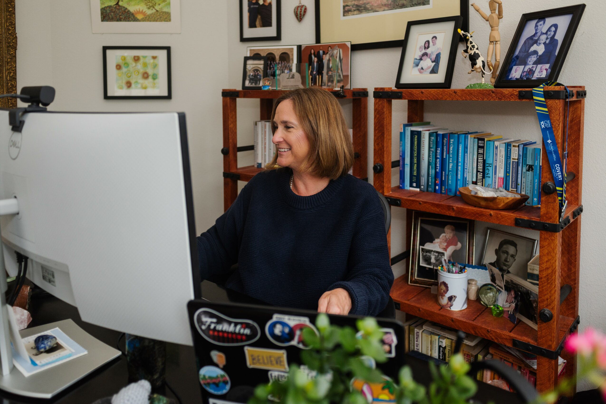 Woman sitting at a desk using a computer in a room with framed pictures and books on shelves