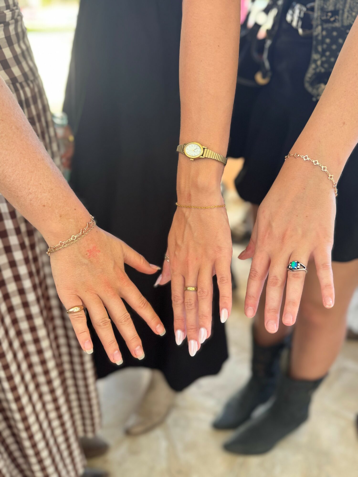 Three hands with rings and bracelets, showing jewelry, against a blurred background of people and clothing.