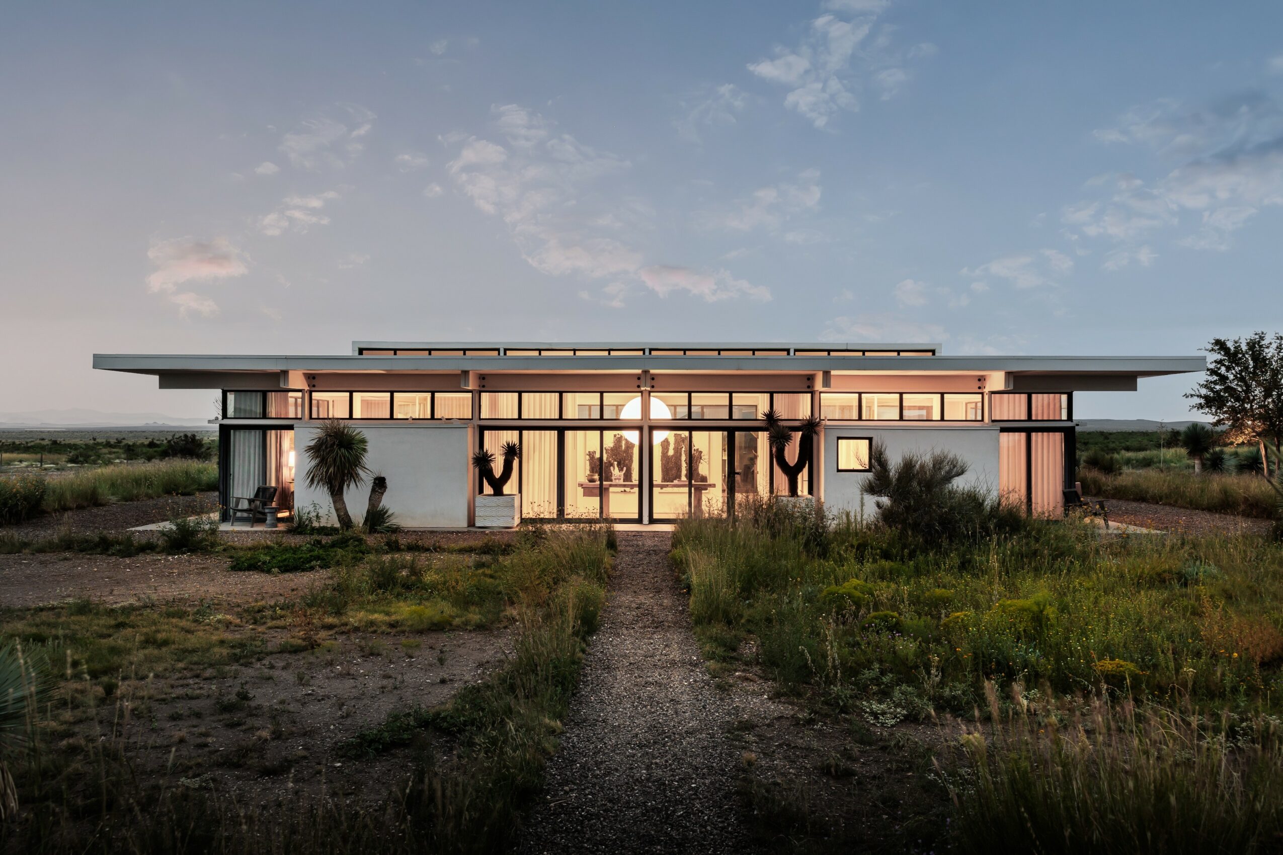 Modern single-story building with large windows, surrounded by natural landscape and a dirt path leading to the entrance.
