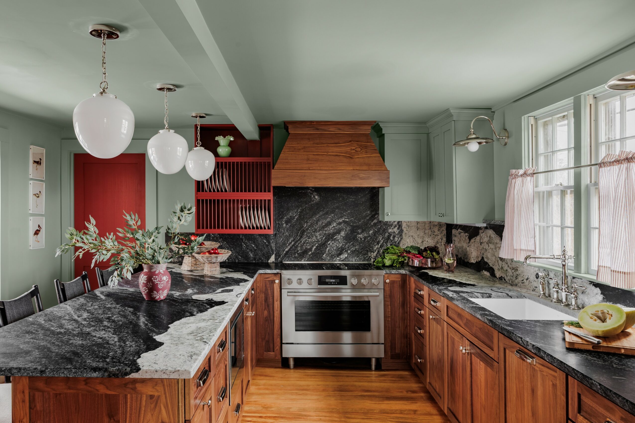 Kitchen with green walls, wooden cabinets, black marble countertops, and a stainless steel oven, with windows and decorative items.