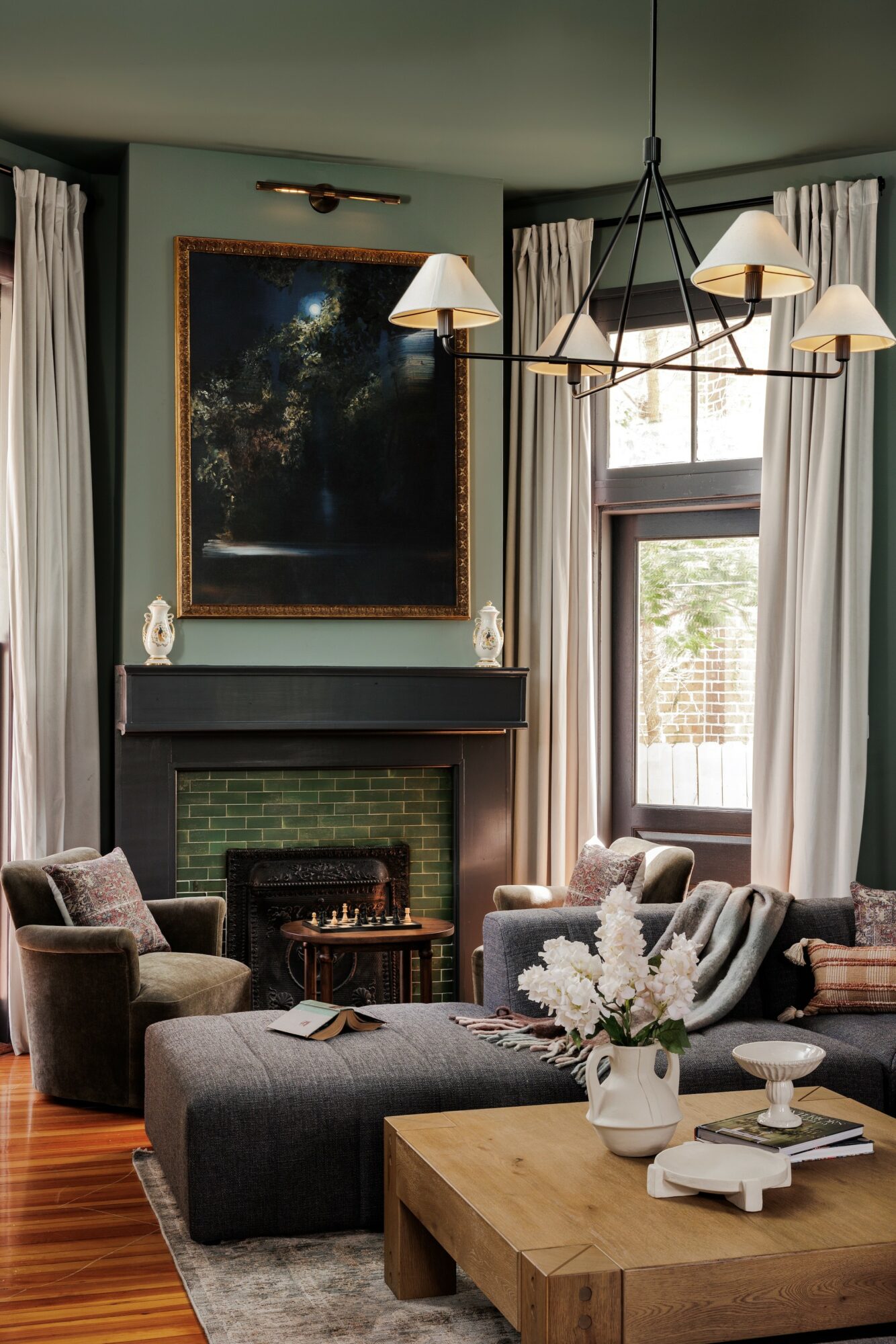 Living room with a fireplace, large window, chandelier, and seating area with cushions and a wooden coffee table.