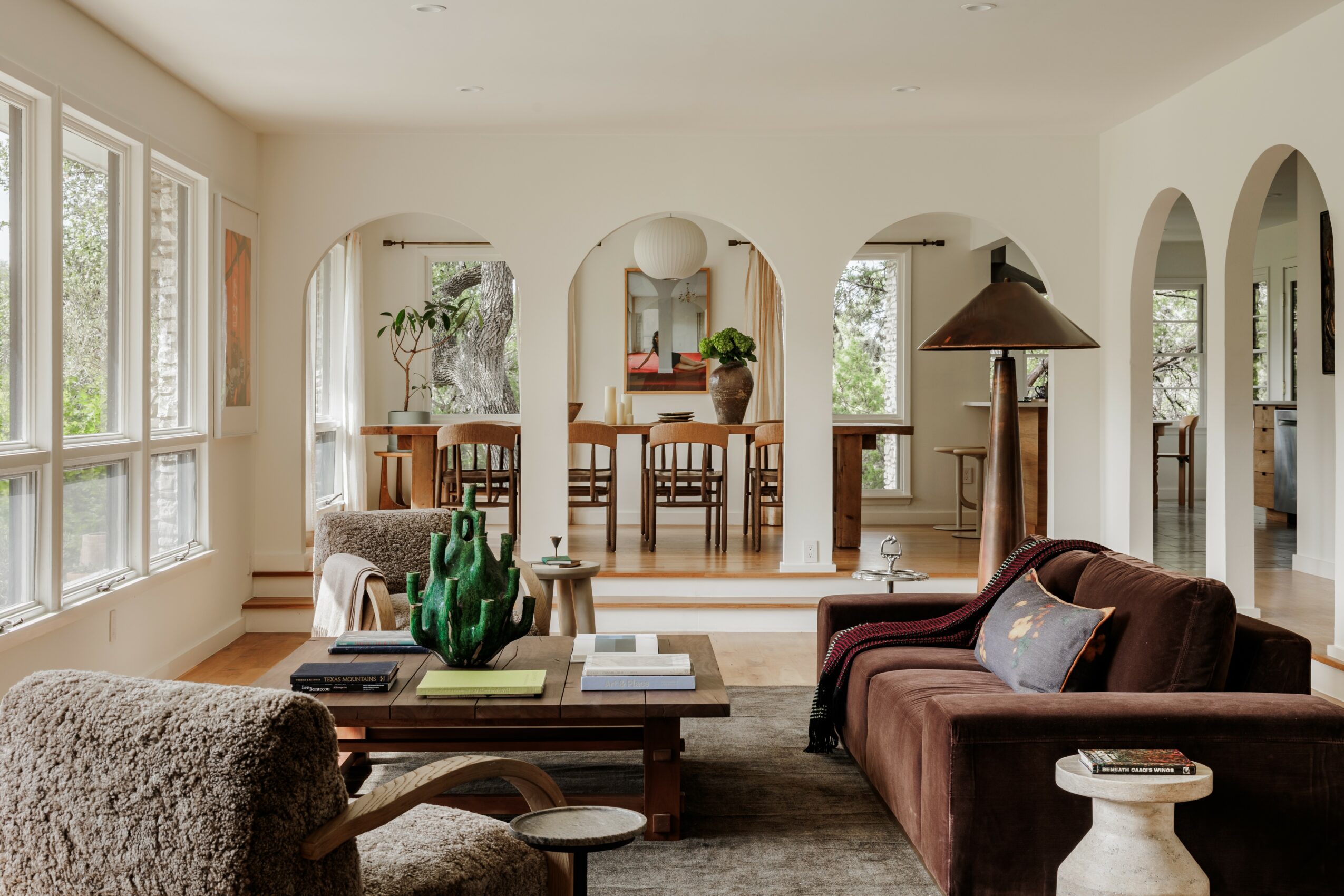 Living room with large windows, sofa, coffee table, and view into dining area with wooden table and chairs.