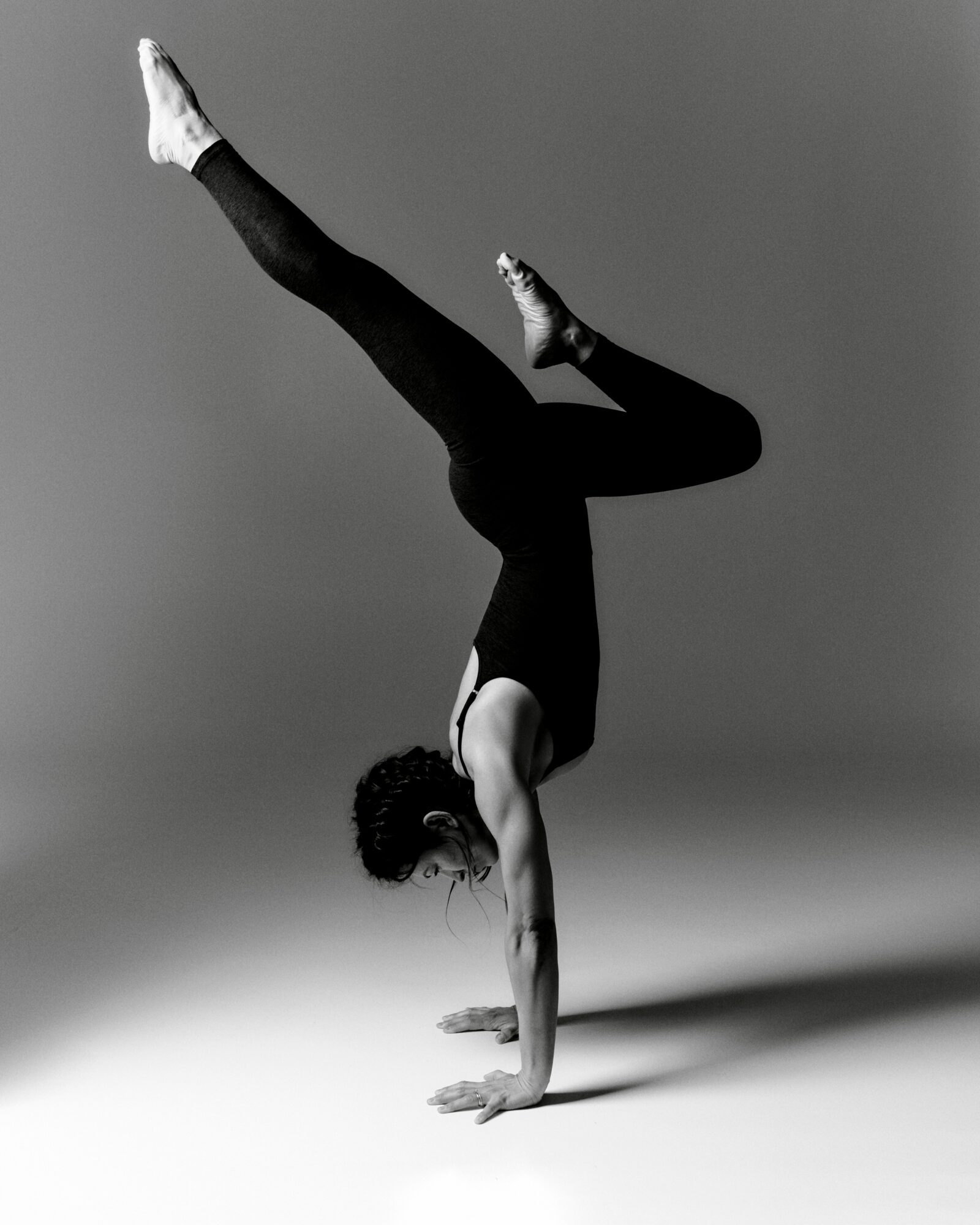 A person balances on one hand with legs extended in a split position against a plain studio background.