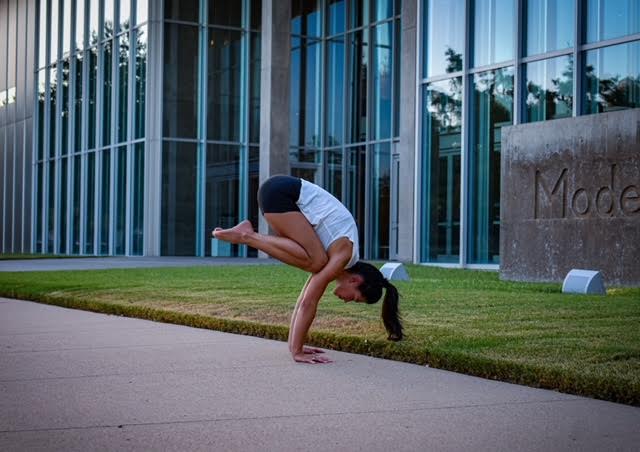 Person balancing in a handstand beside a glass building and a stone sign.
