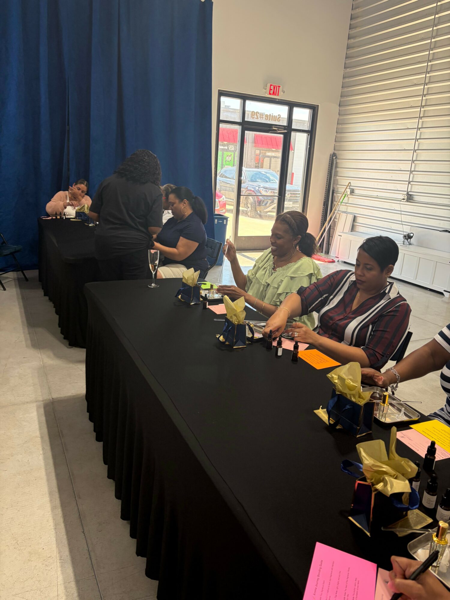 People standing around a table with yellow and pink papers, in a room with a window and blue curtains.