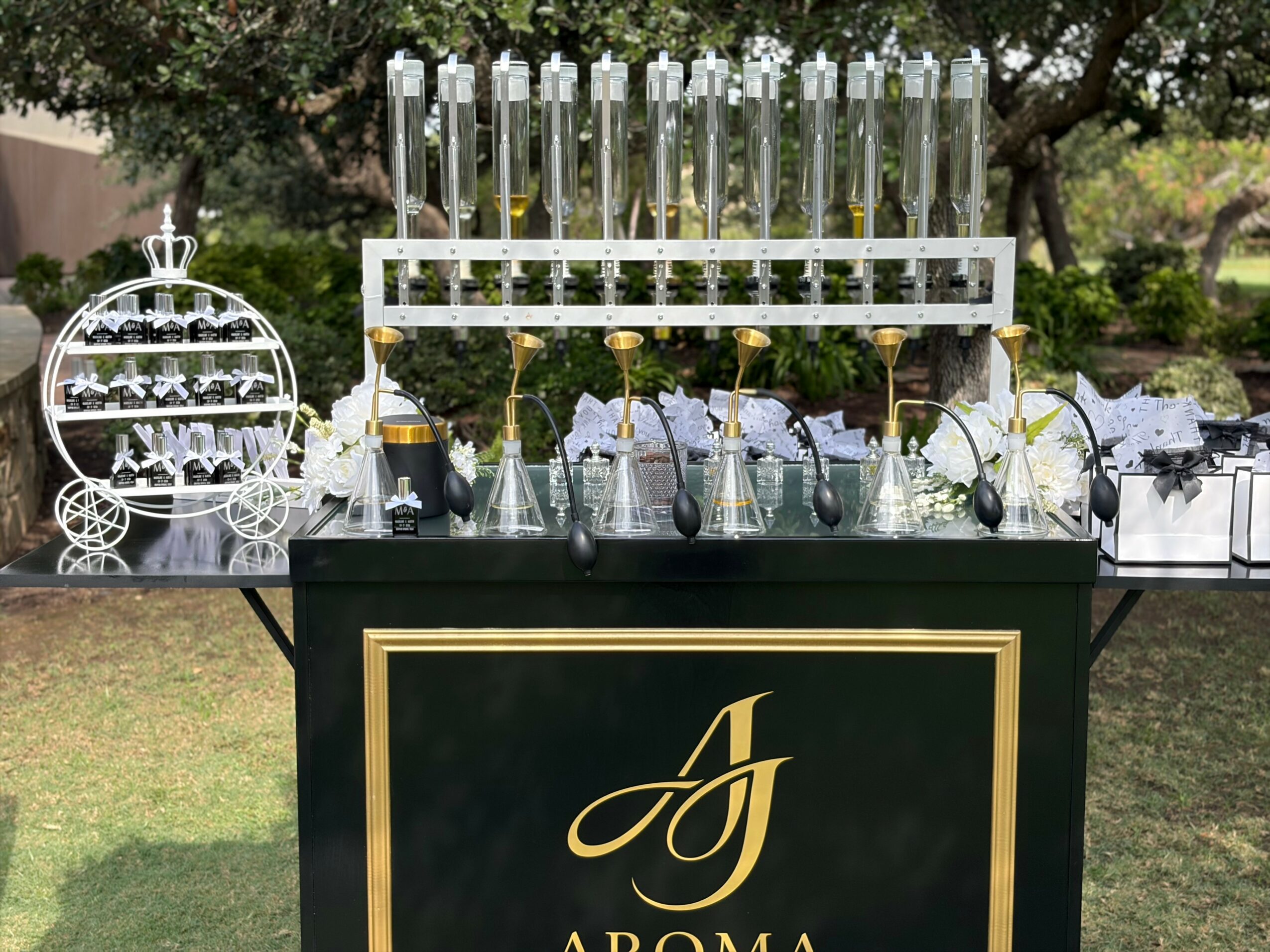Bar setup with glassware, bottles, and decorative items outdoors, featuring a black and gold sign with a stylized letter 'A'.