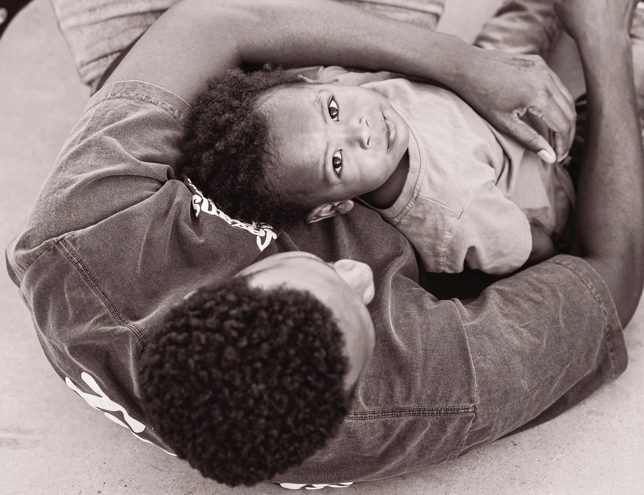 Two children lying on the floor, one resting head on the other's chest, looking at the camera.