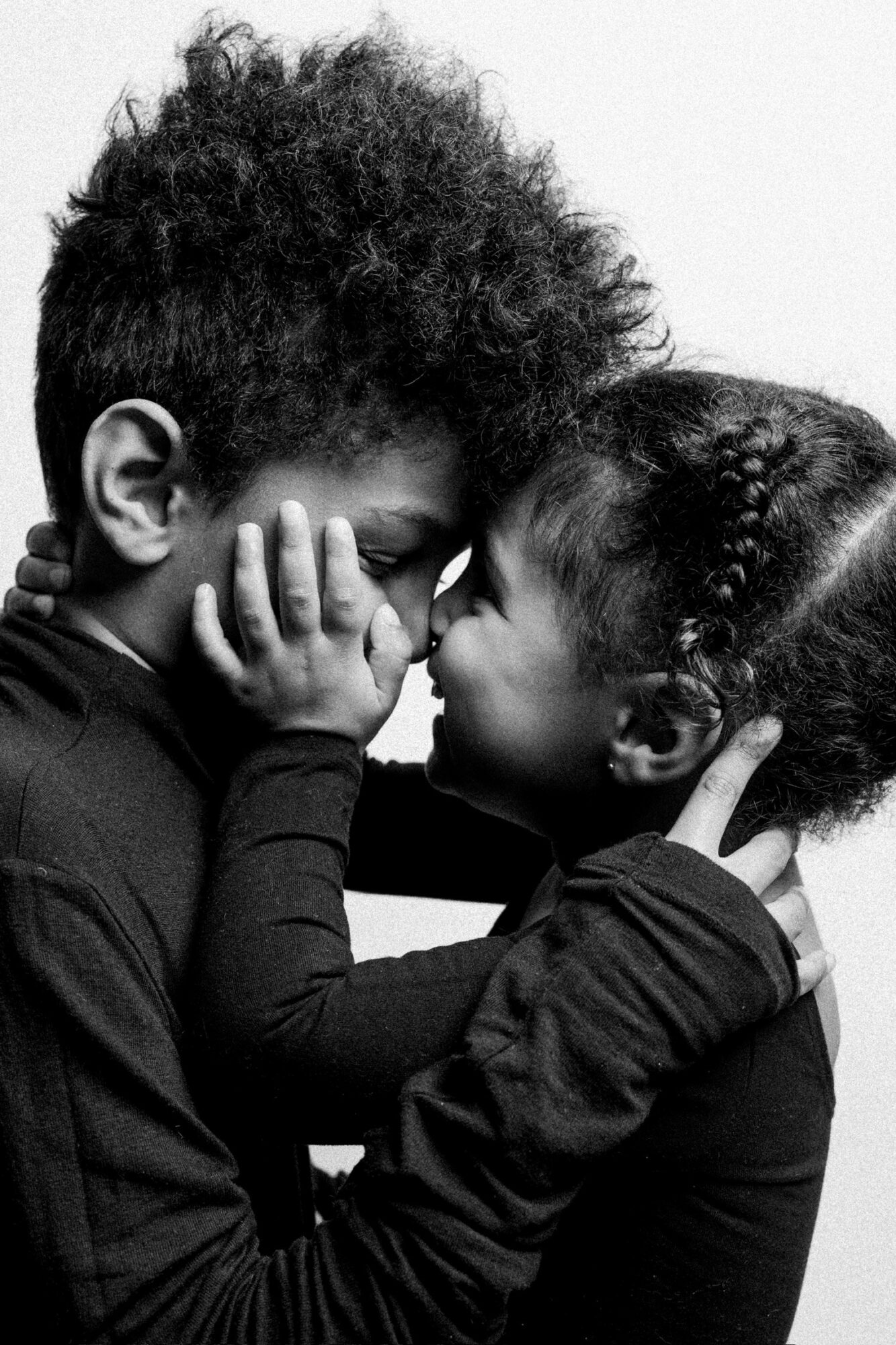 Two children face each other closely, touching foreheads and holding each other's faces, in black and white.