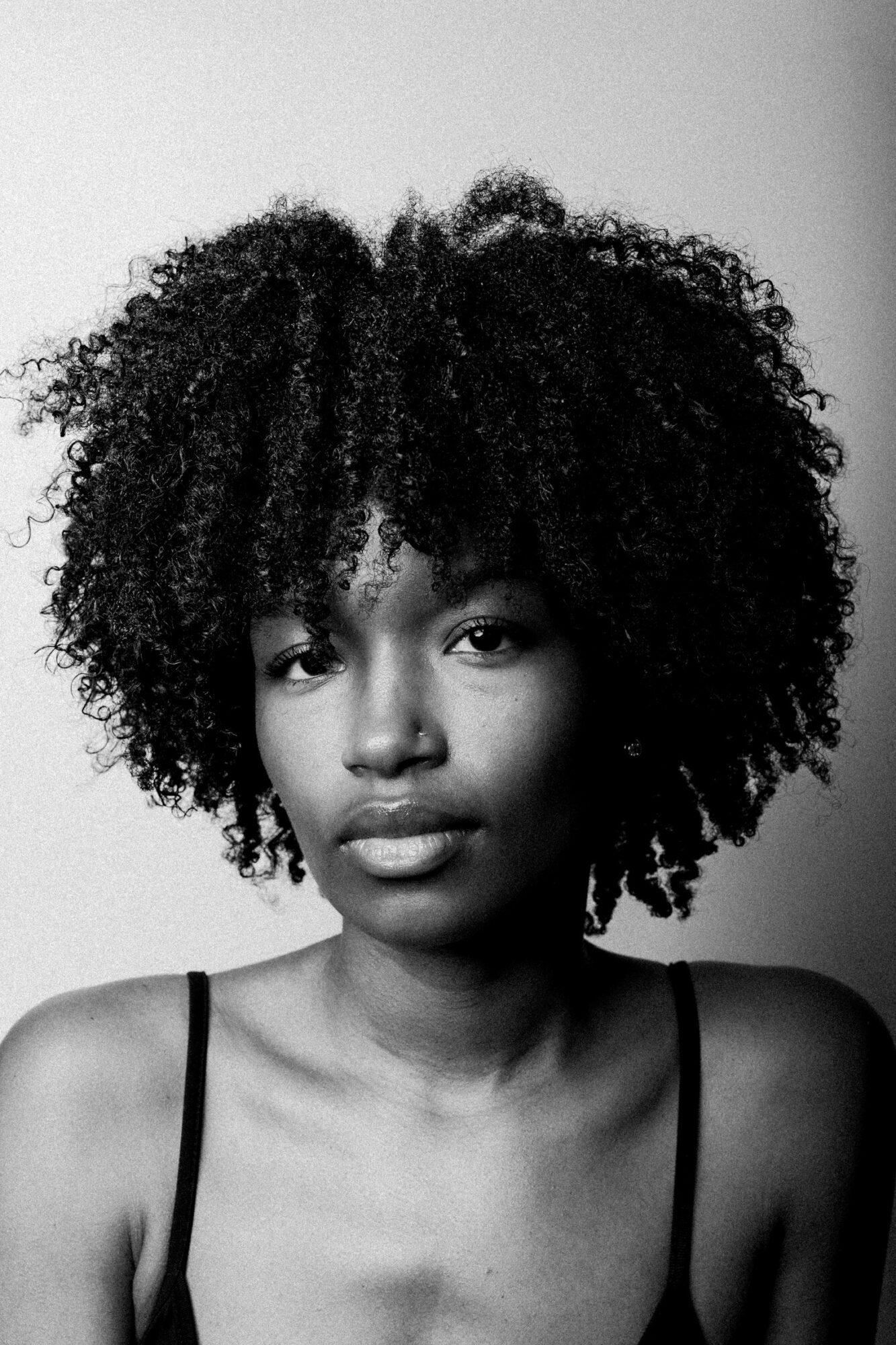 Black and white portrait of a woman with natural curly hair, looking at the camera with a neutral expression.