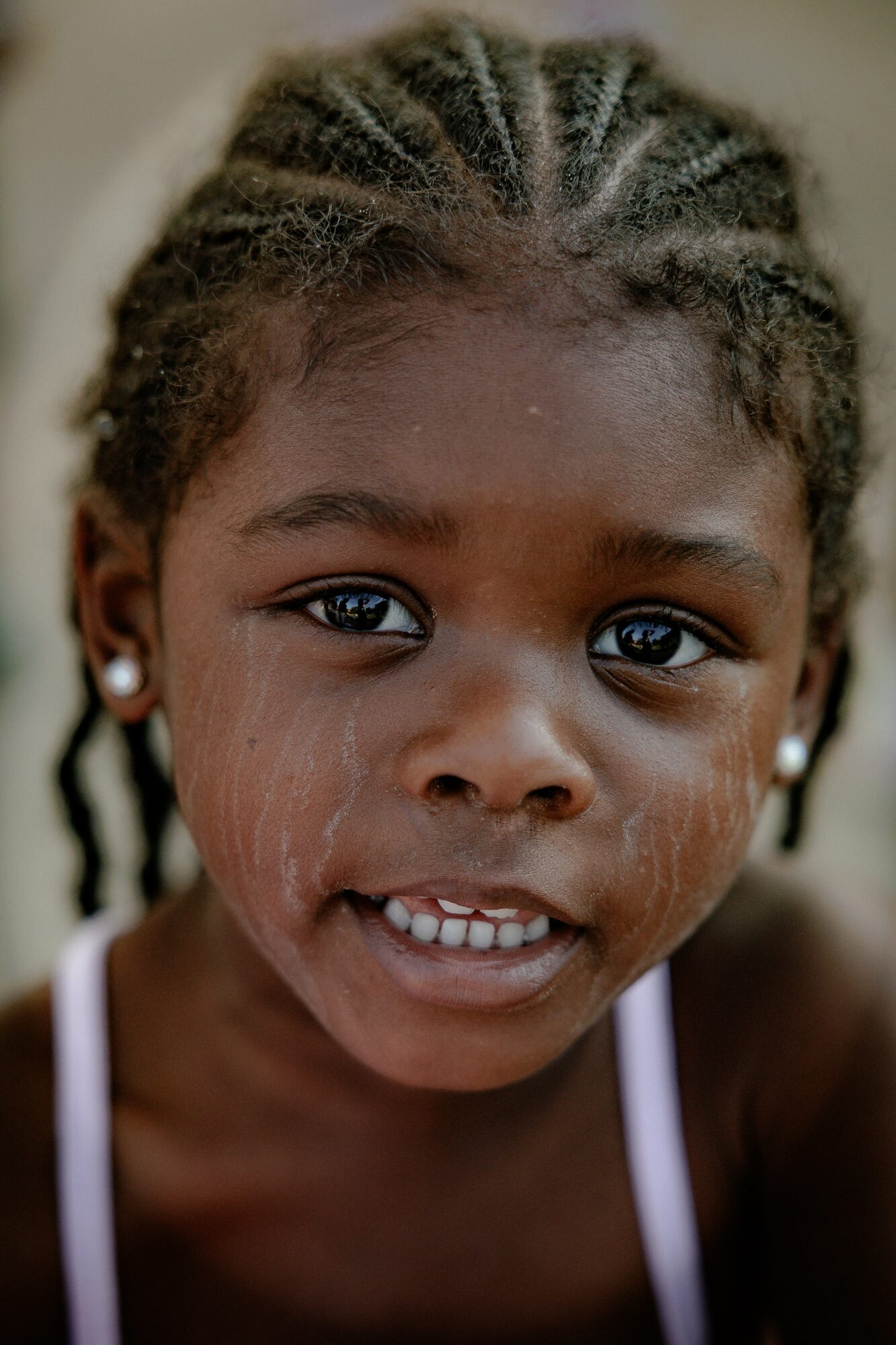 Close-up of a young girl with braided hair, earrings, and a neutral expression, looking directly at the camera.