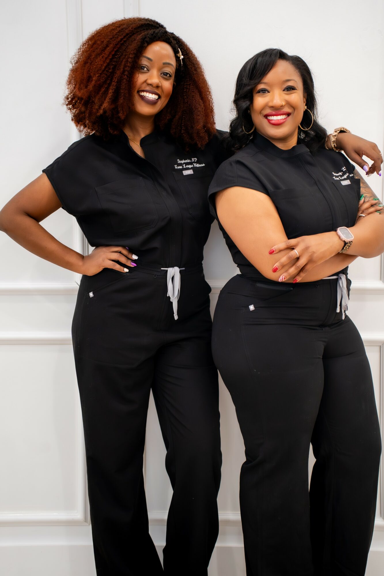 Two women in black uniforms standing side by side, smiling, with one woman resting her arm on the other's shoulder.