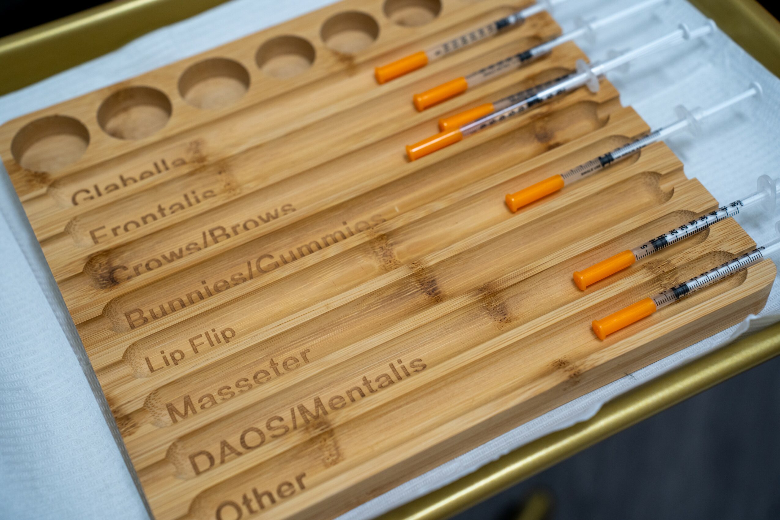 Set of dental tools with orange handles in a wooden tray labeled with different dental procedures, viewed from above.