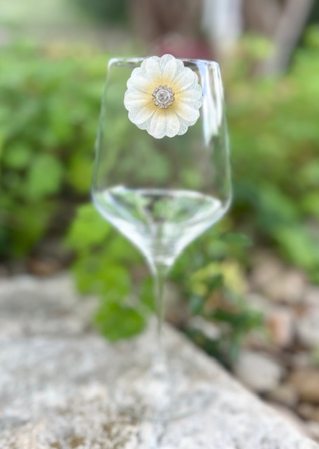 Empty wine glass with a white flower attached, outdoors with green foliage background.
