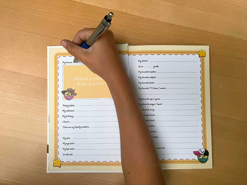 Person writing in a colorful notebook with lined pages on a wooden surface.