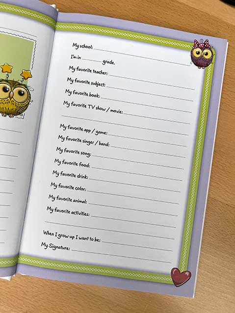 Open notebook with lined pages, decorated with owl and heart stickers, on a wooden surface, filled with handwritten school-related prompts.