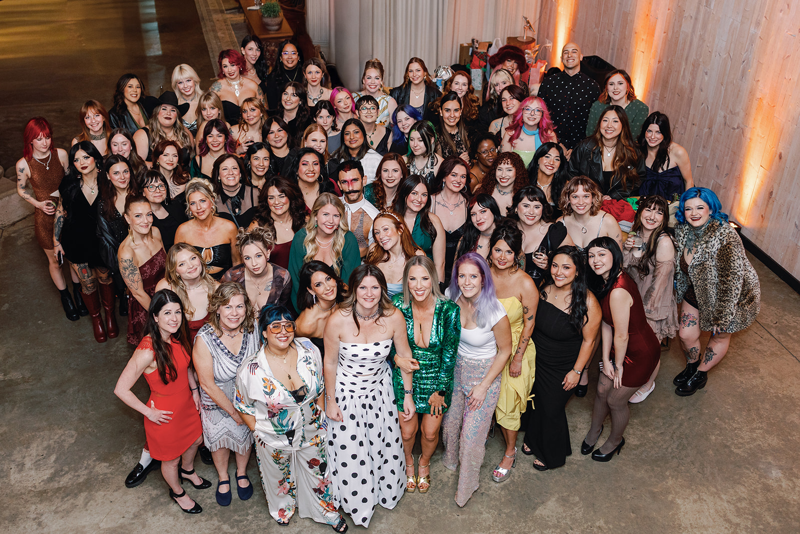 Large group of women and girls gathered indoors, posing for a photo, with some smiling and others serious.