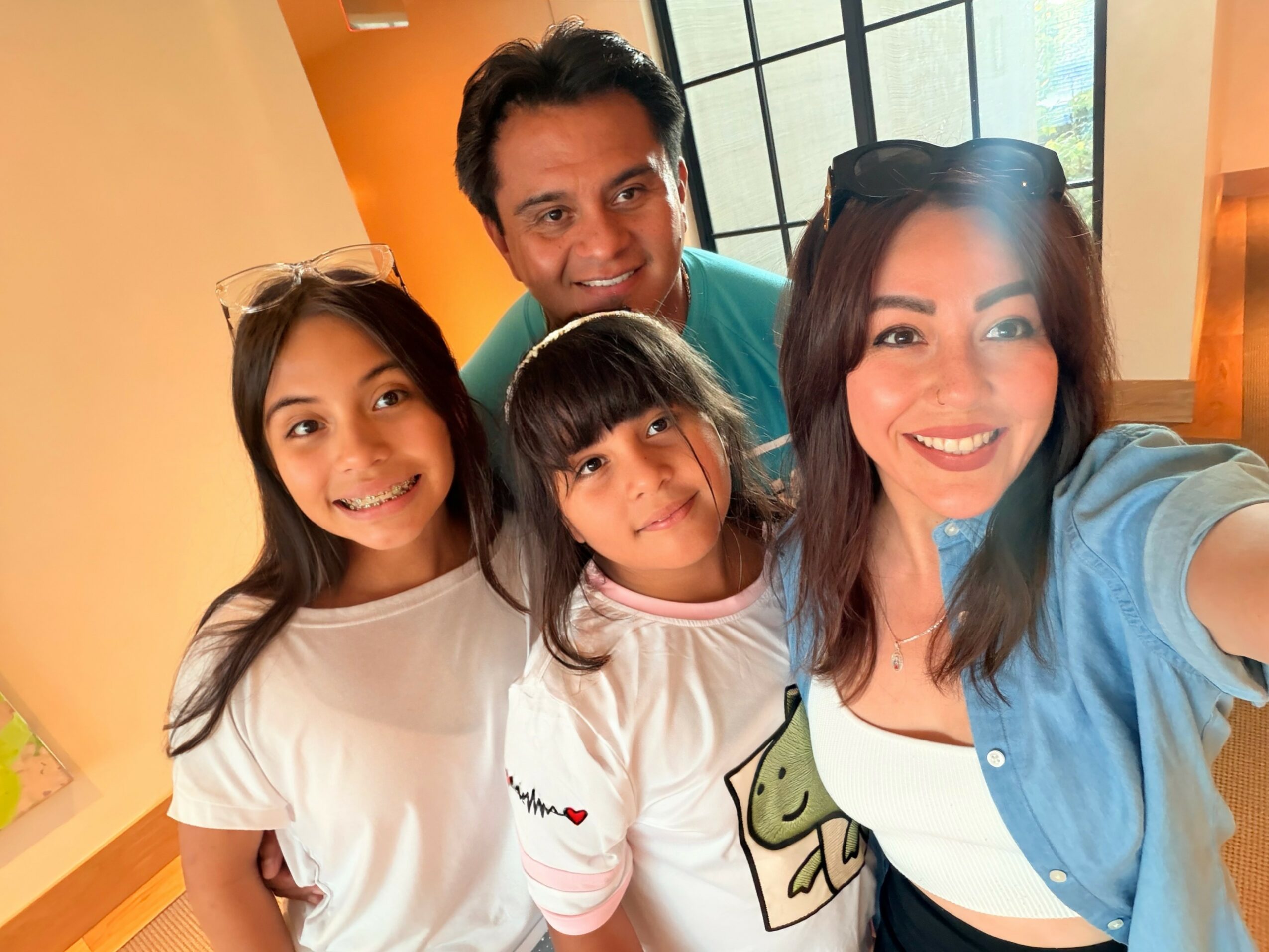Four people smiling indoors, two adults and two children, with a window in the background.