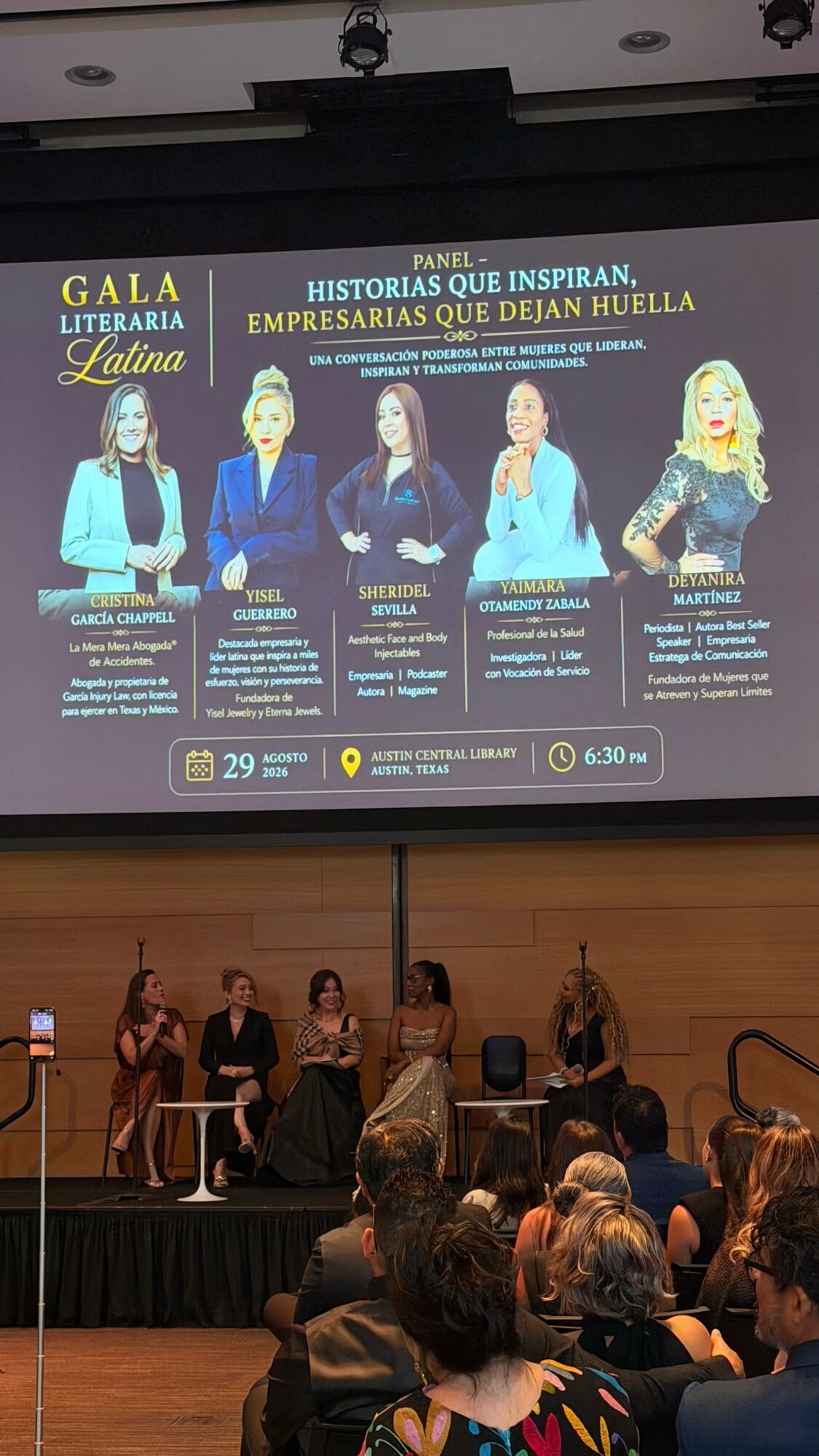Large screen displays five women with text about inspiring stories and entrepreneurs, audience seated in front, stage with people standing.