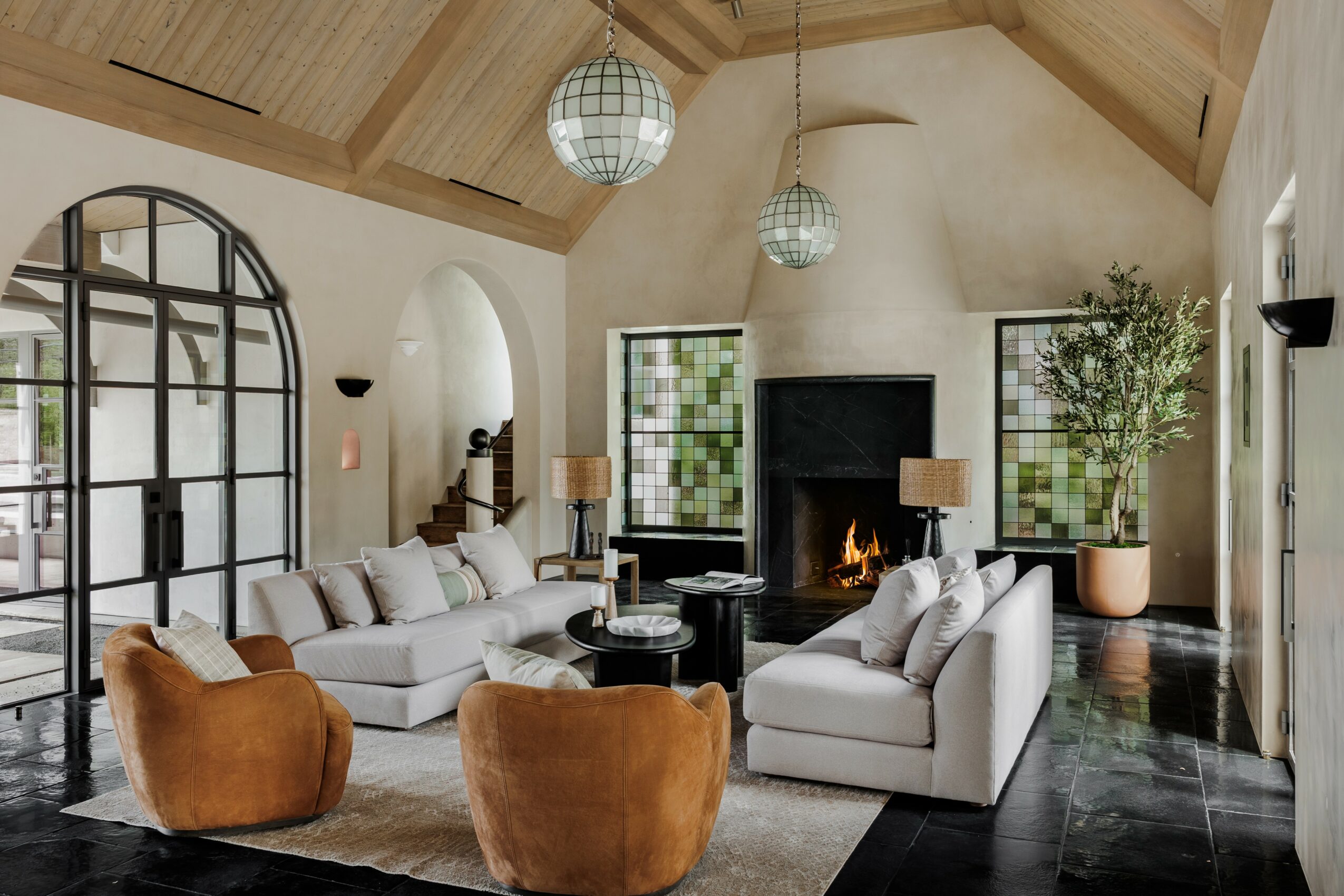 Living room with white sofas, two brown chairs, a fireplace, large windows, and a high wooden ceiling with hanging lights.