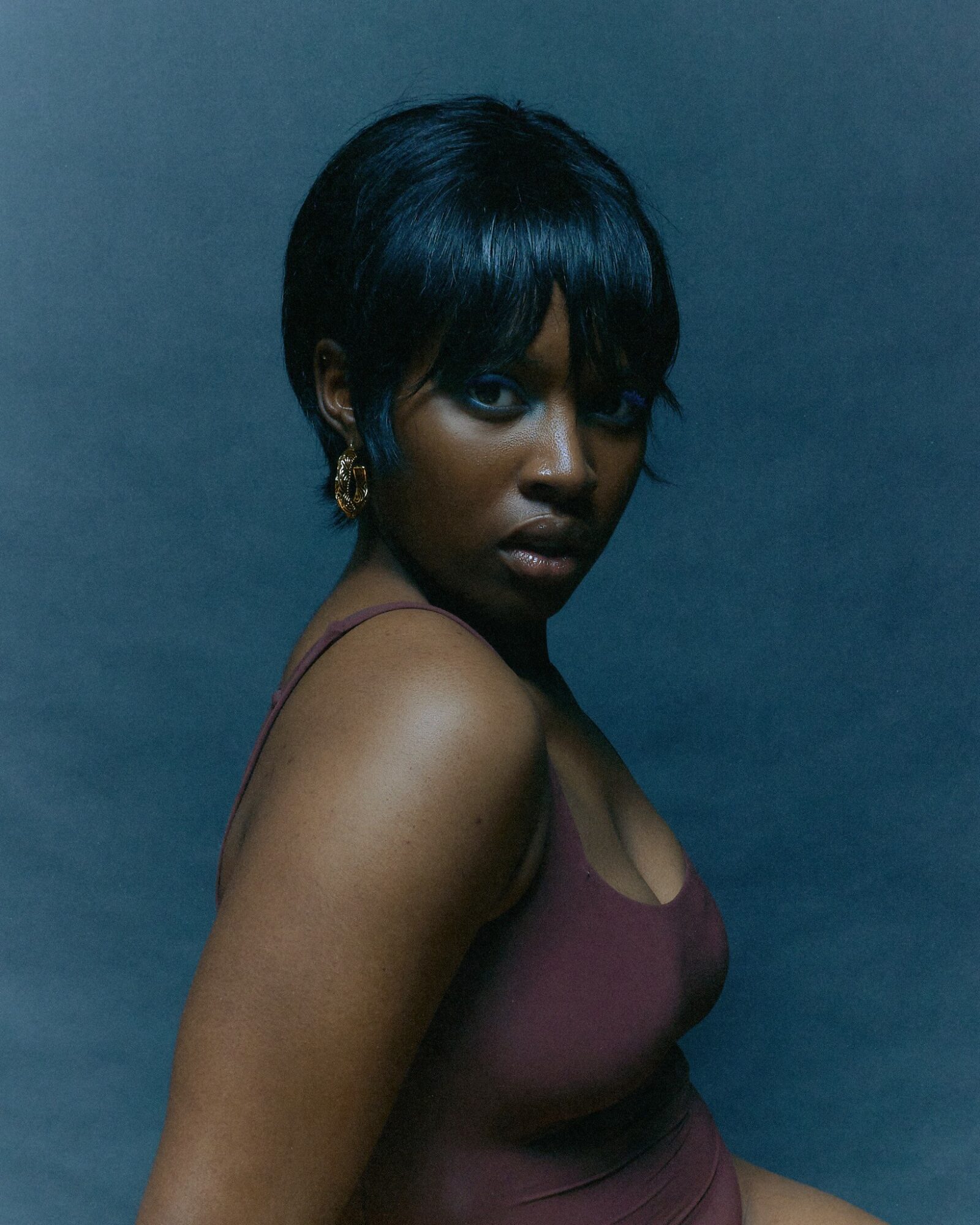 Portrait of a woman with short black hair, wearing a sleeveless top, looking at the camera against a dark background.