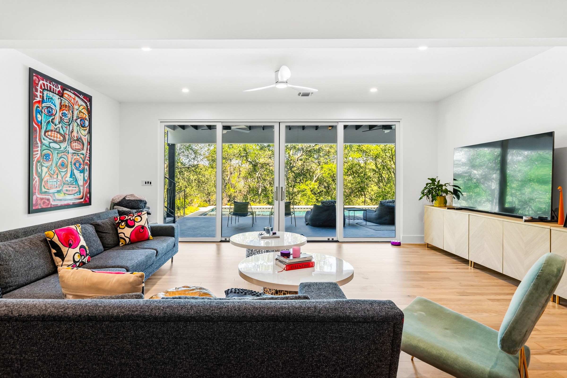 Living room with large glass doors, a sofa, a chair, a TV, and artwork on the wall, bright and modern.