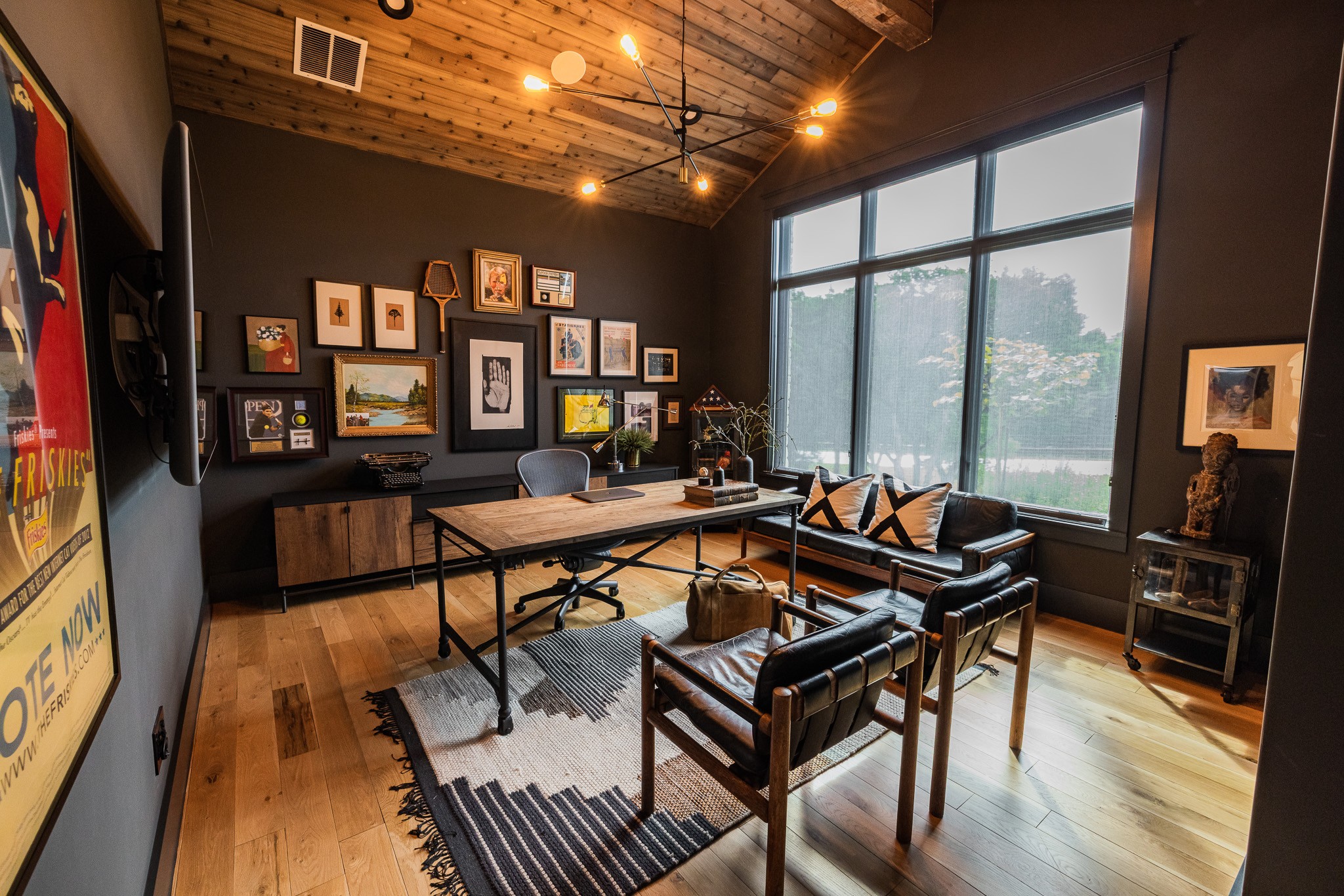 Modern living room with black walls, large window, wooden ceiling, and a mix of chairs and a sofa around a coffee table.
