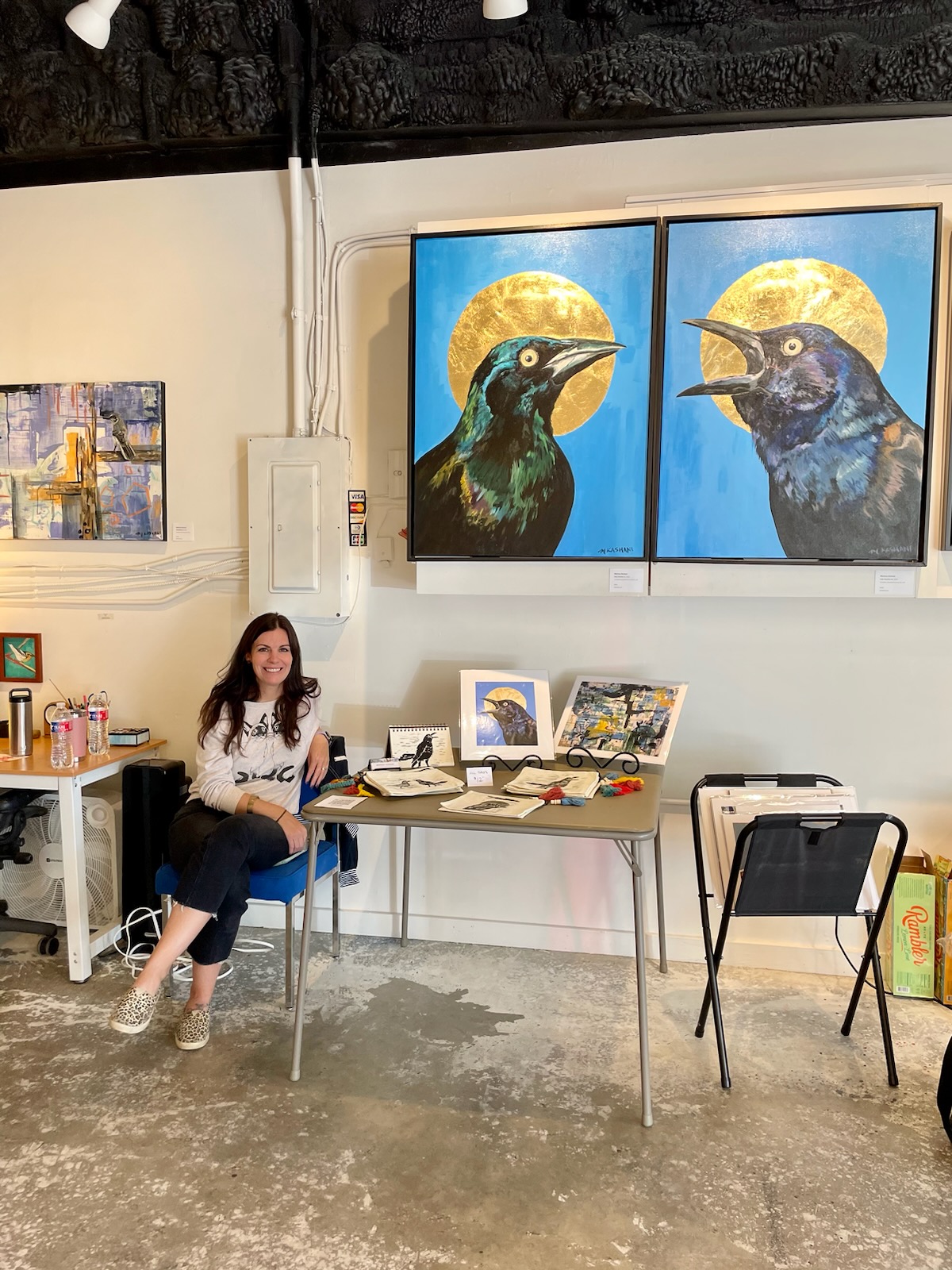 Woman sitting on a chair in an art gallery with paintings of birds on the wall behind her.