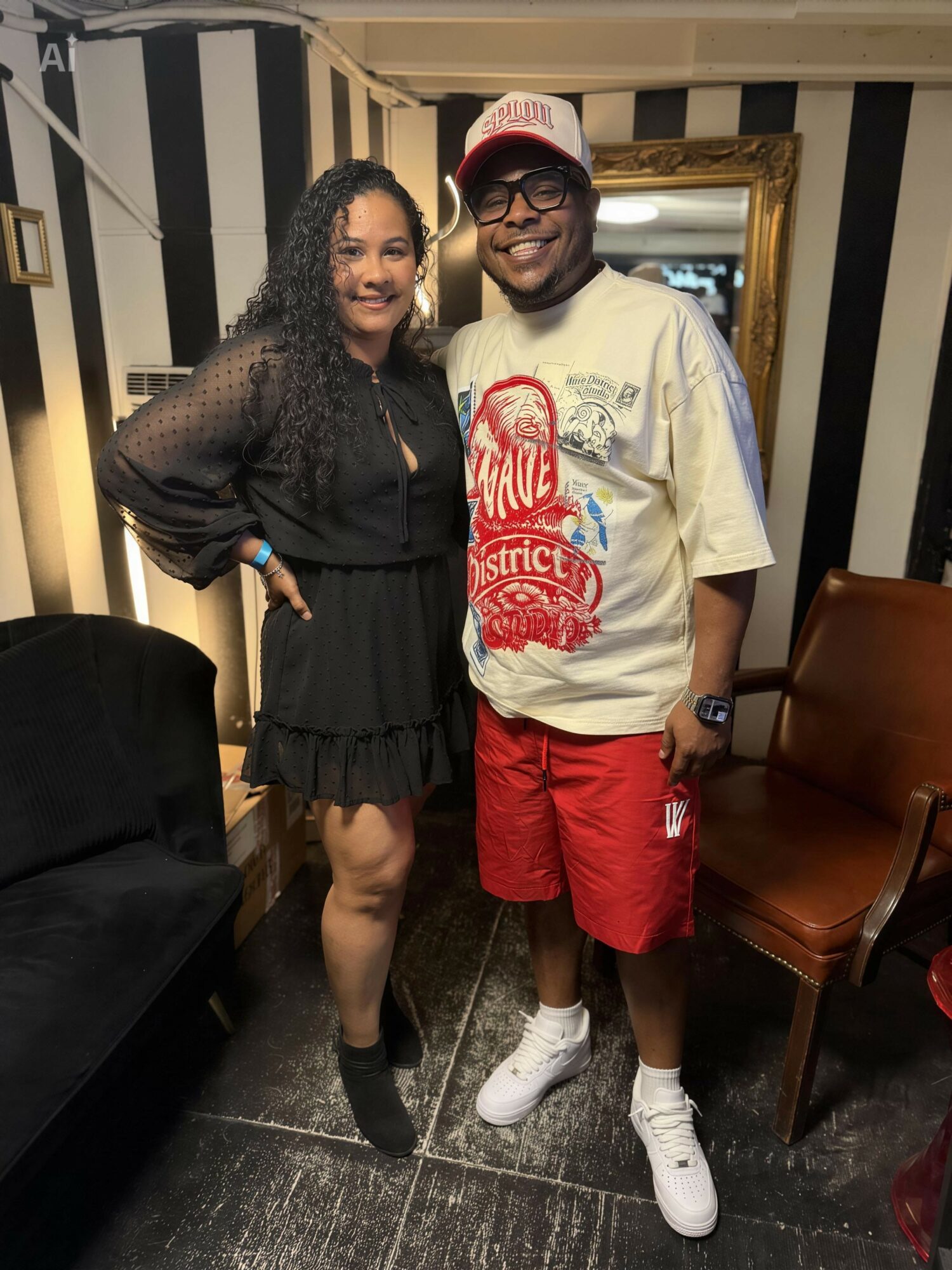 Two people standing indoors, smiling, with black and white striped walls and furniture around them.