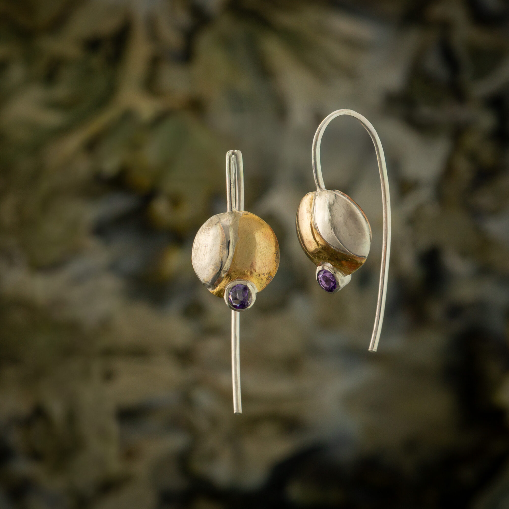 Gold earrings with purple gemstones hanging against a blurred background.