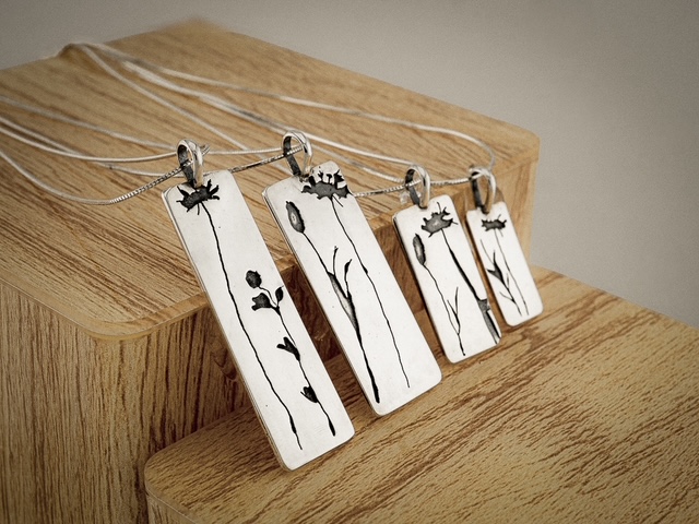Four rectangular metal pendants with floral engravings hang from thin chains on a wooden surface.