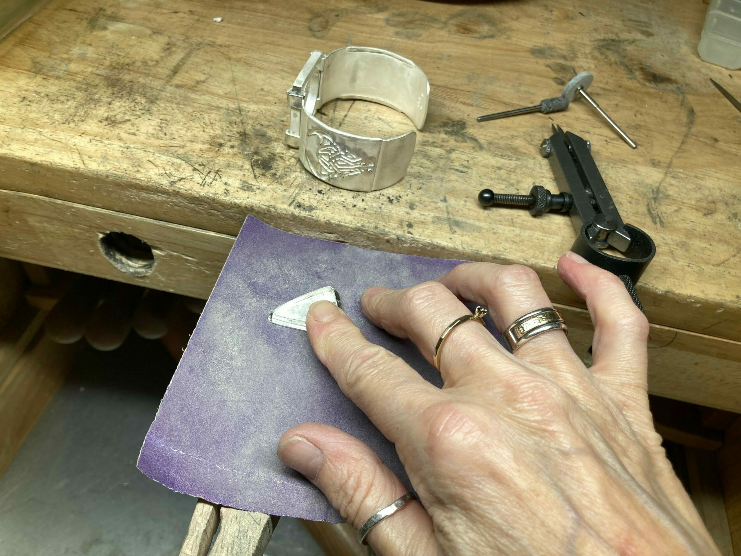 Hand holding a purple cloth, working on a wooden surface with tools and a glass object, possibly a workshop scene.