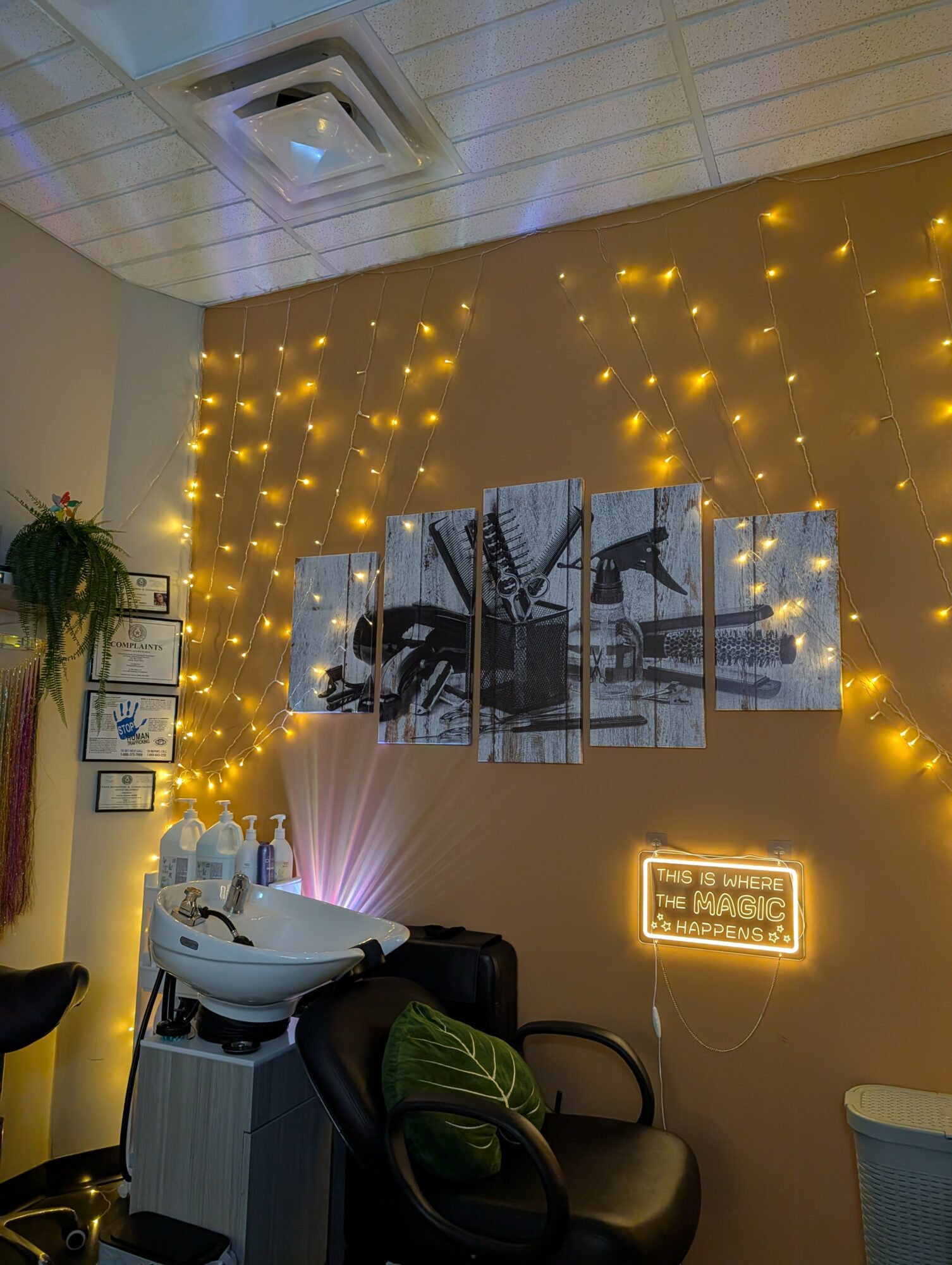 Salon with wall art, fairy lights, a neon sign, and a hair washing station with a black chair and green pillow.