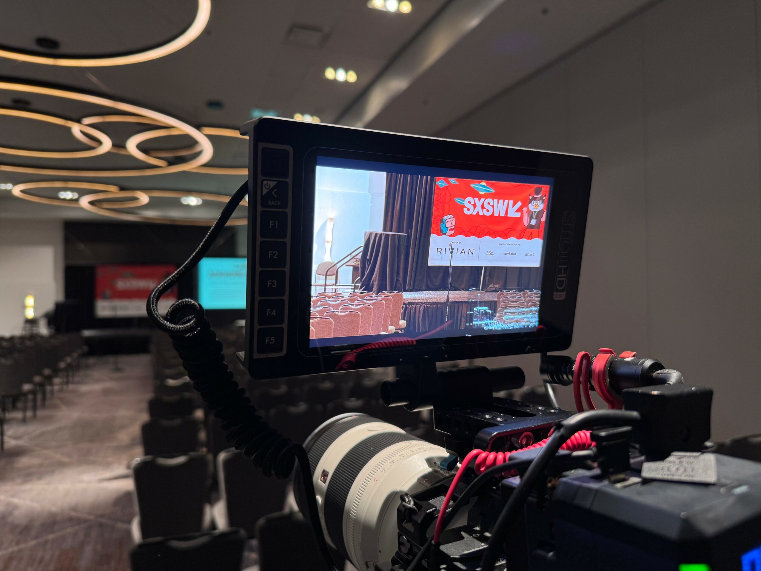 Camera monitor displaying a stage with a red banner and chairs, in an indoor conference room.